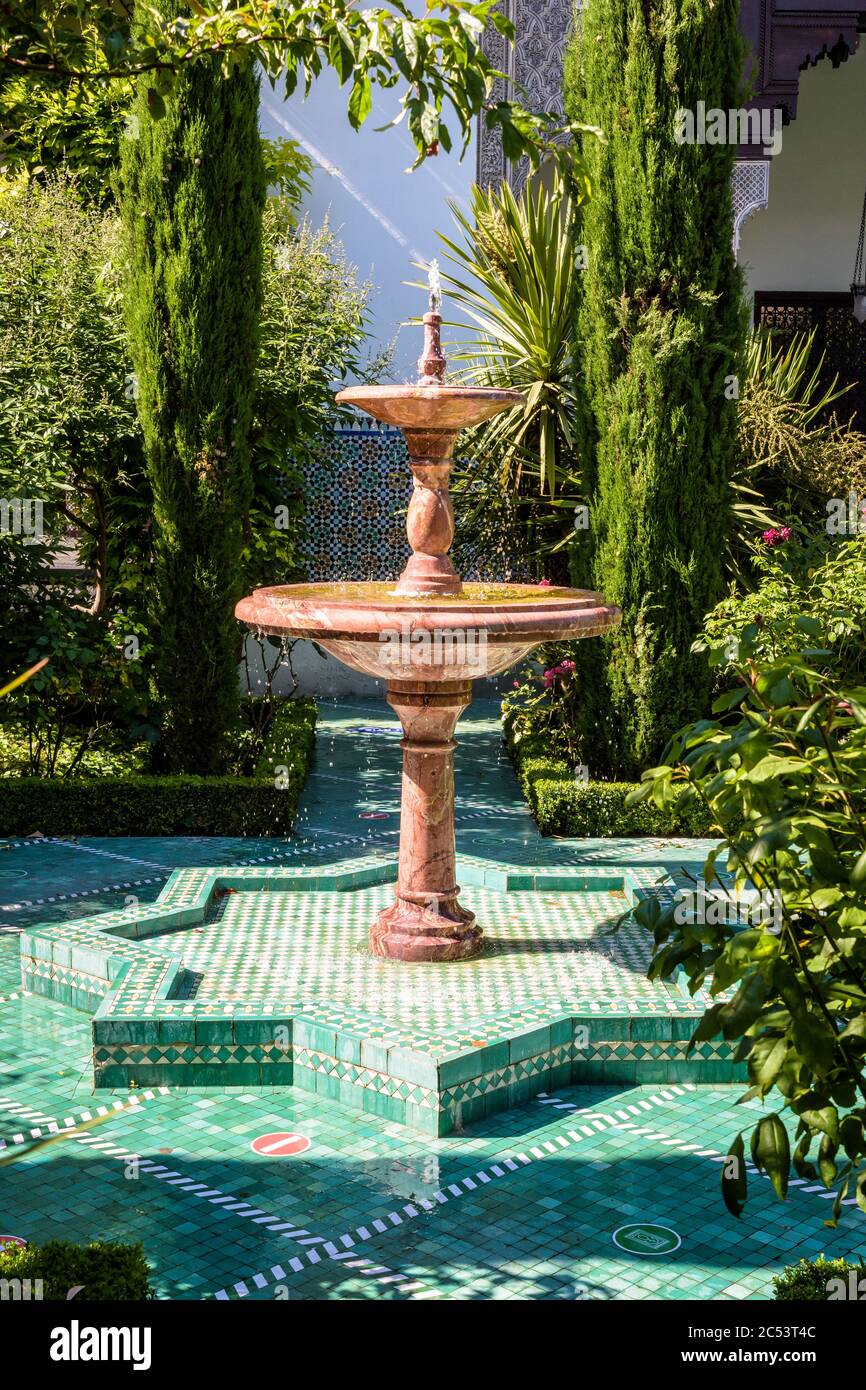 Una fontana di marmo marrone in un vicolo coperto da piccole piastrelle verdi nel lussureggiante giardino della Grande Moschea di Parigi. Foto Stock
