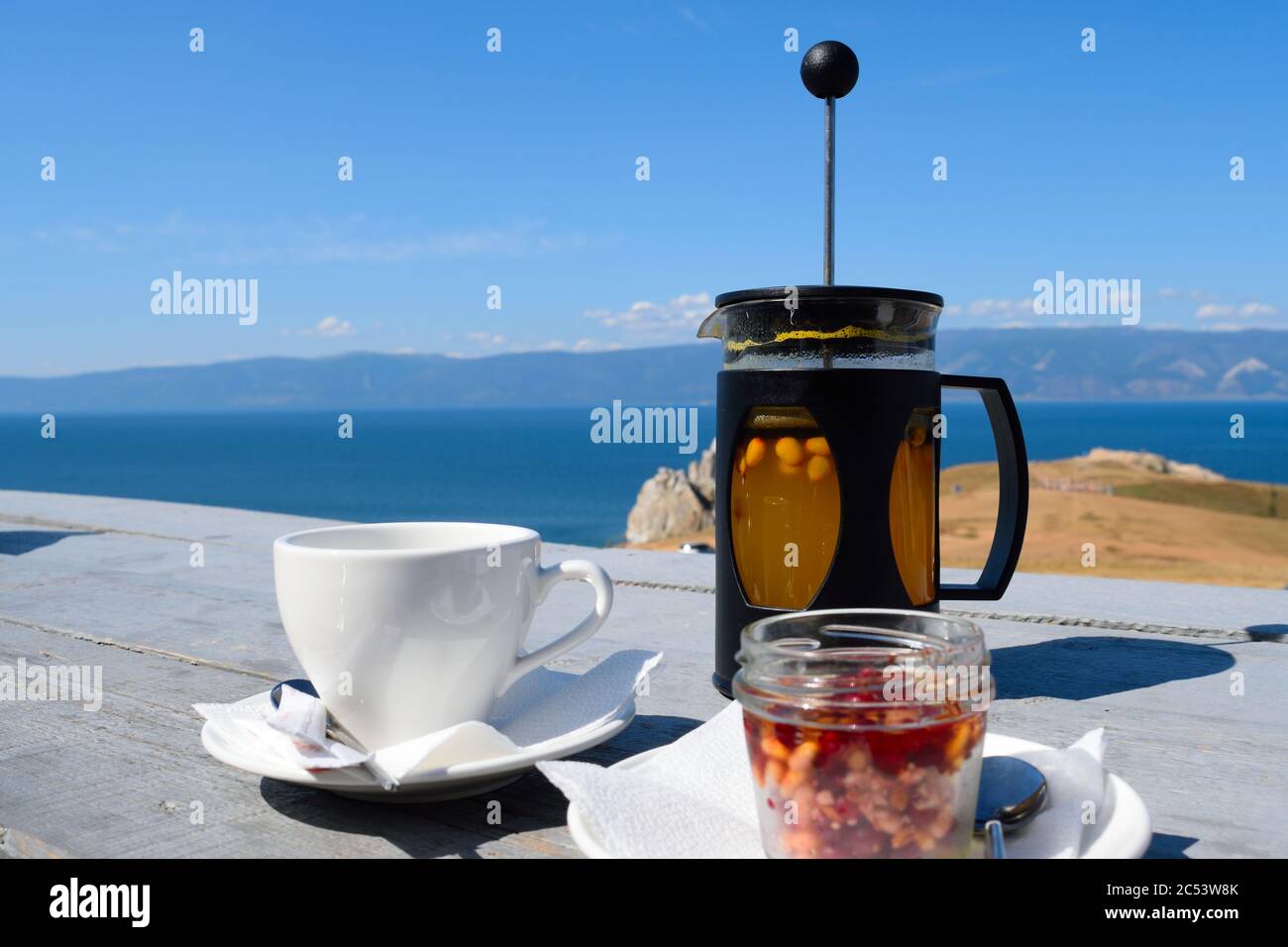 Tè e deserto con una vista: Tè e miele di fibbiano di mare, noce di pino e dessert di frutti di bosco rossi con vista della roccia di Shaman sull'isola di Olkhon, lago Baikal, Russia Foto Stock