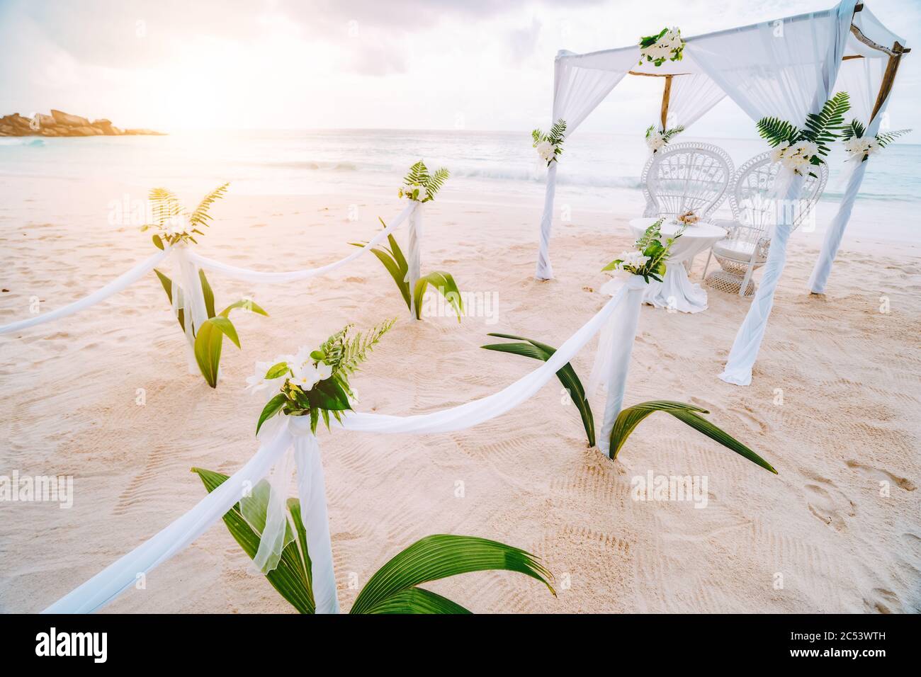 Decorato romantico ambiente per matrimoni con tavolo e sedie sulla spiaggia tropicale sabbiosa al tramonto, le isole Seychelles. Foto Stock