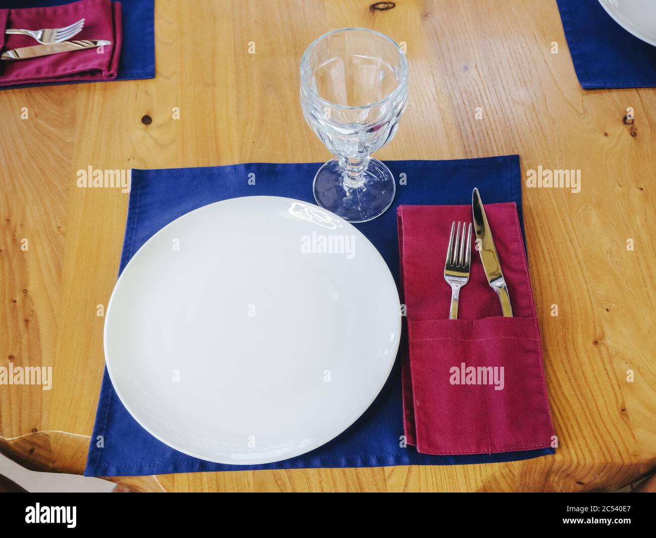 Piatto bianco con una forcella in cristallo e coltello su un tovagliolo blu su un tavolo di legno chiaro. Nuove posate lucide. Foto di primo piano Foto Stock