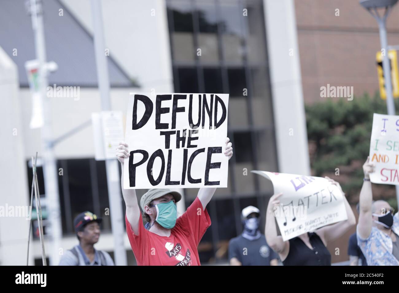 Un uomo visto tra una folla di manifestanti BLM che sostengono un poster che dice Defund the Police Foto Stock
