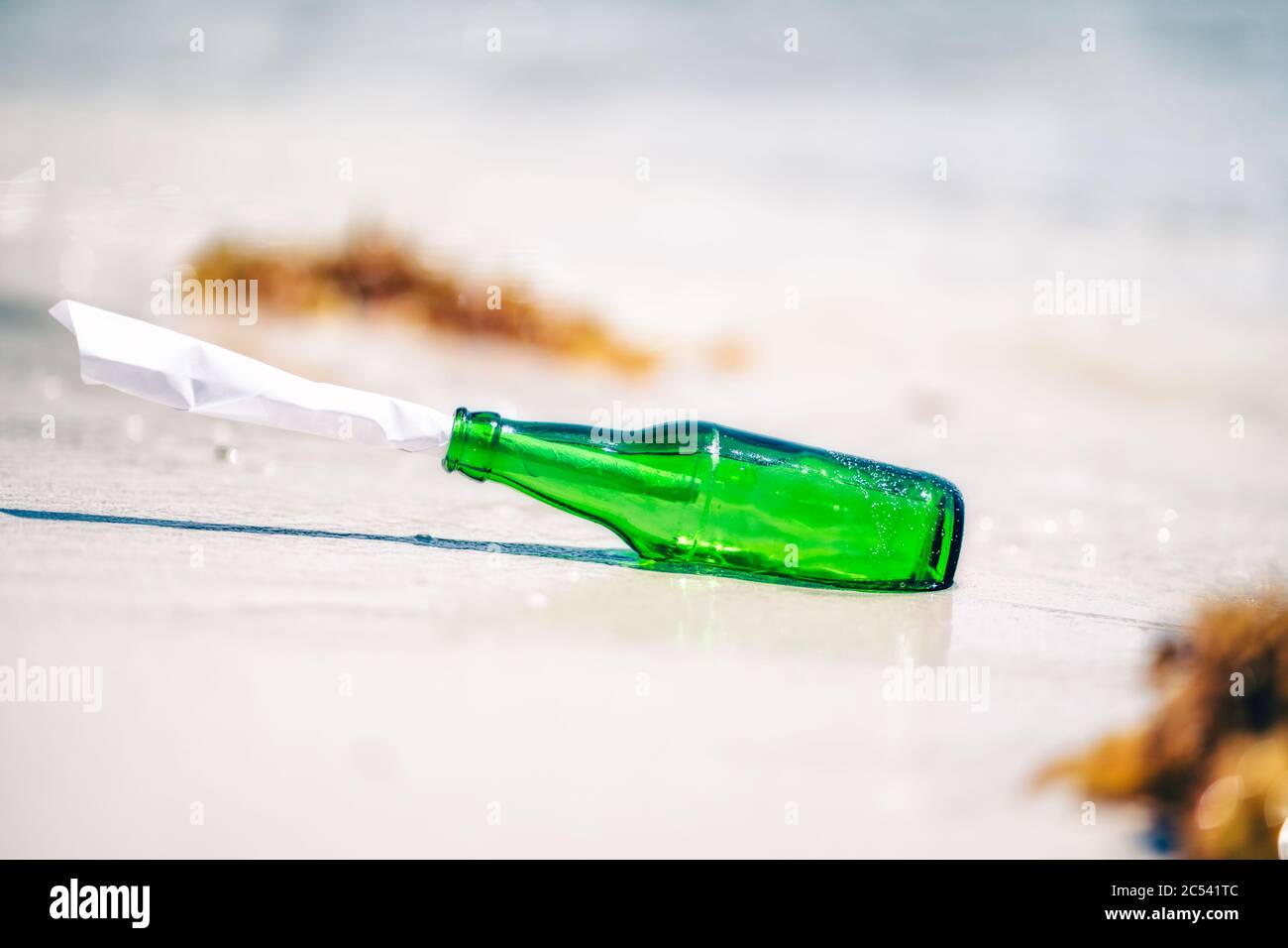 Bottiglia verde con messaggio di carta adagiato su una spiaggia di sabbia bianca. Foto Stock