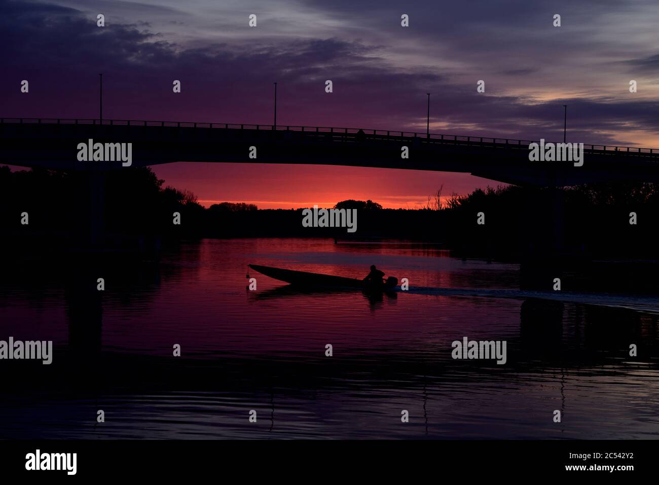Alba colorata, silhouette di un pescatore e barca a vela sotto il ponte. Foto Stock