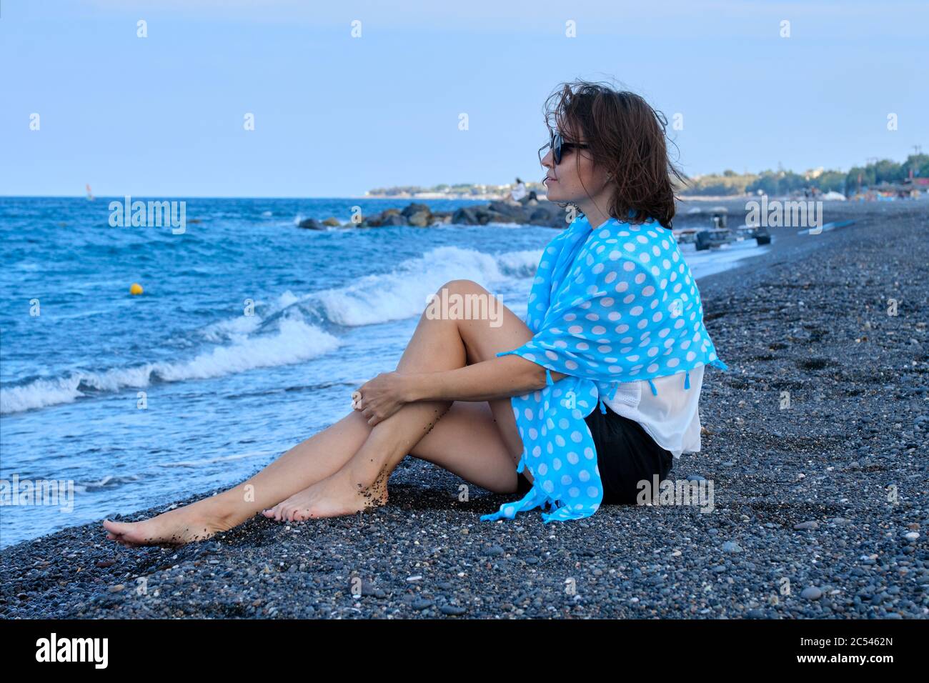 Donna di mezza età seduta sulla spiaggia di mare, in viaggio felice riposo donna guarda al mare Foto Stock