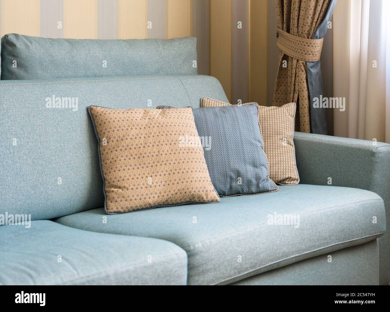 Divano o divano con cuscini all'interno della casa. Primo piano con cuscini classici. Particolare dell'interno color pastello di appartamento nella luce del giorno. Foto Stock