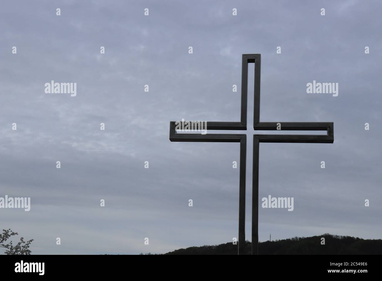 Una croce cattolica in metallo costruita su un parco commemorativo e un cielo nuvoloso sullo sfondo fotografato dal basso Foto Stock