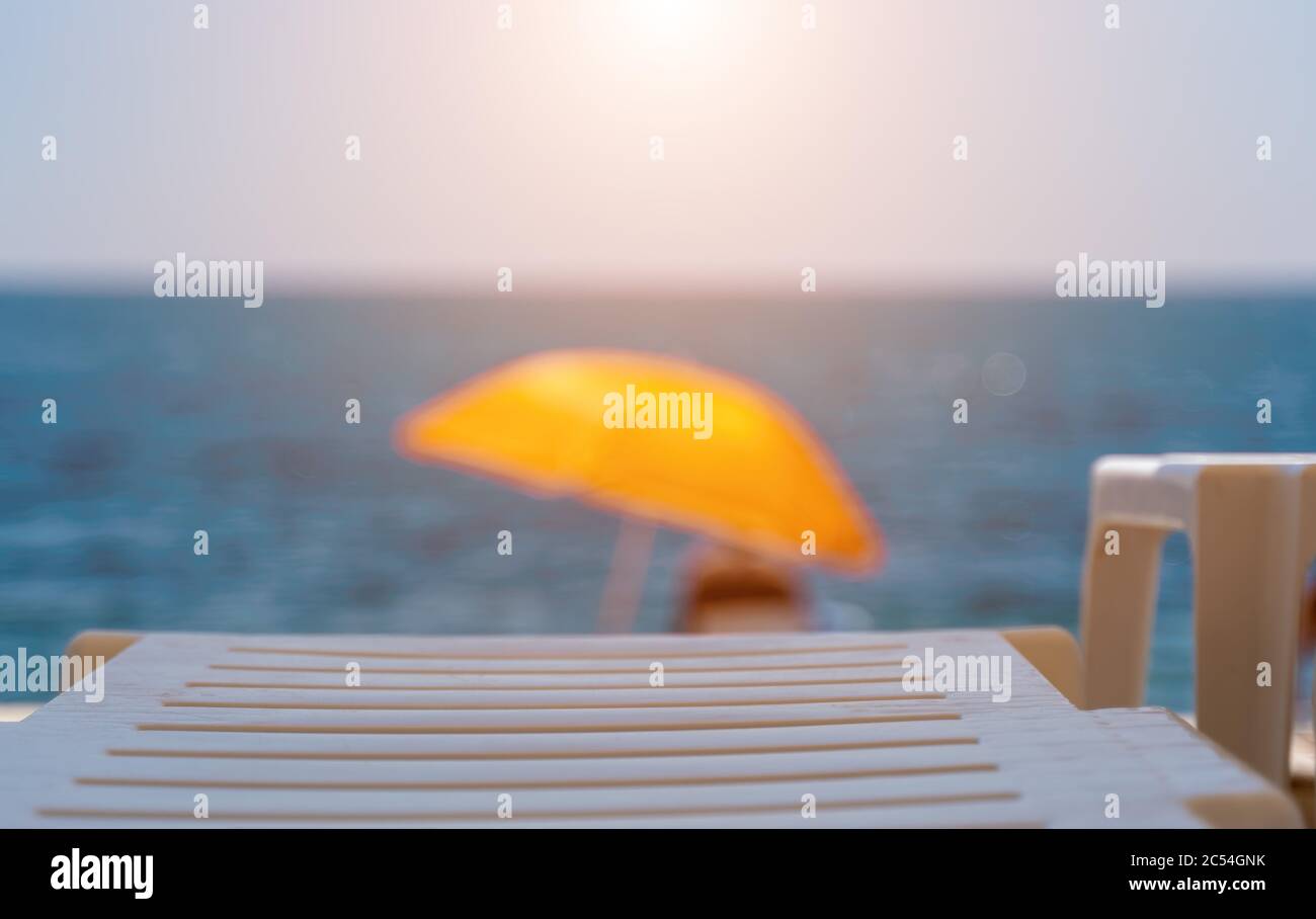 Messa a fuoco selettiva. Destinazione estiva per le vacanze, ombrelloni e lettini arancioni sulla spiaggia rocciosa vuota con mare sullo sfondo. Vacanze e turismo Foto Stock
