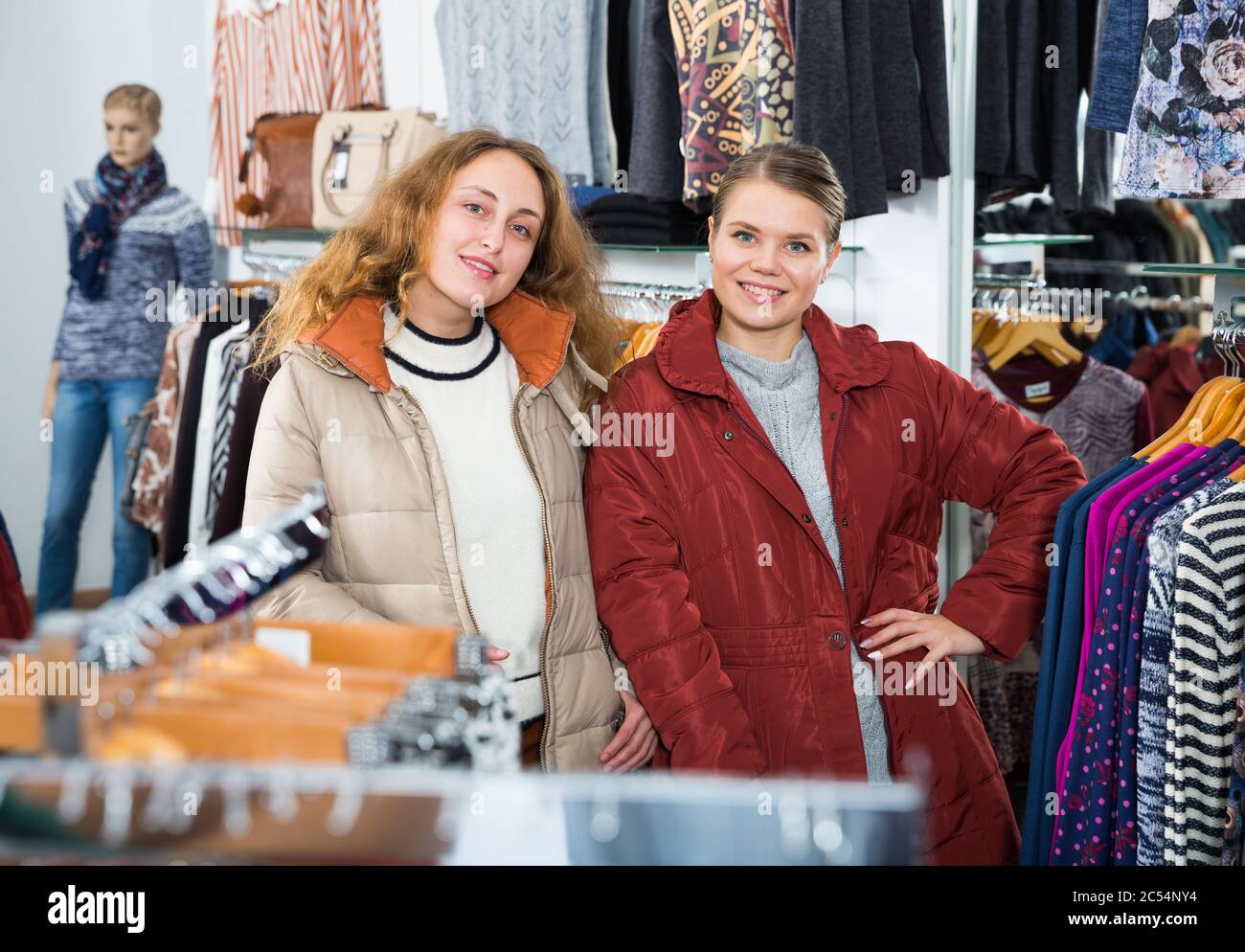 Due giovani donne positive in posa di cappotti in cappotti boutique di abbigliamento Foto Stock