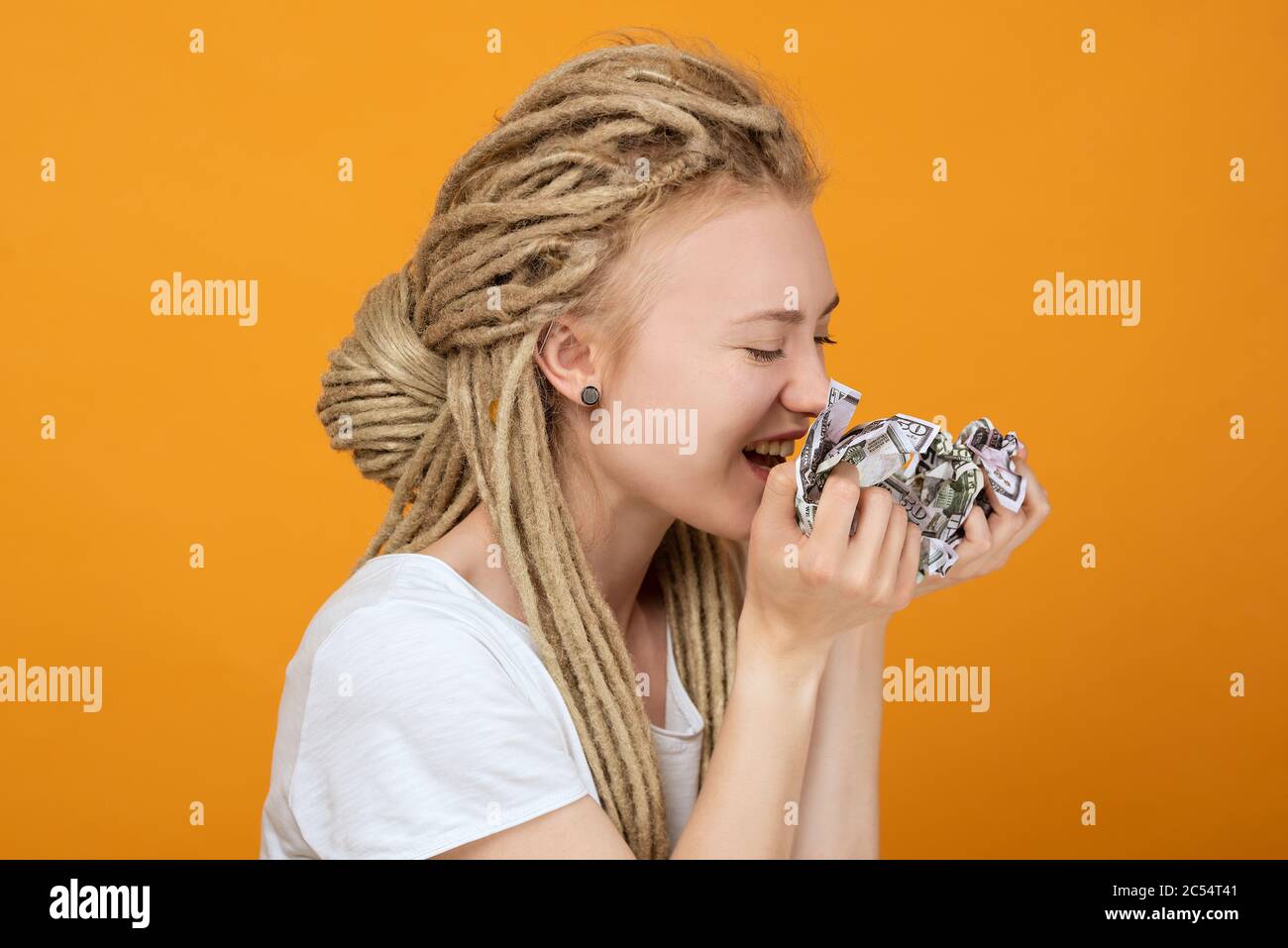 la ragazza tiene i soldi sminuzzati e vuole mangiarli, umore giocoso, acconciatura insolita, dreadlock bianchi Foto Stock