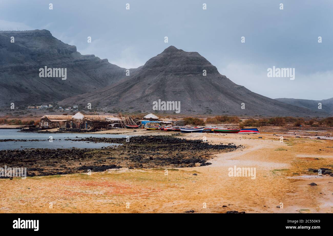 Misterioso paesaggio di costa sabbiosa con villaggio di pescatori e montagne vulcaniche nere sullo sfondo. Baia Das Gatas. A nord di Calhau, Sao Vicente I. Foto Stock