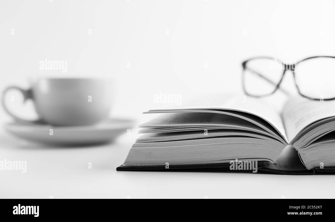 Libro aperto, tazza di tè caffè e bicchieri da lettura su sfondo bianco. Imparare da casa. Cura di sé, tempo lontano dalla tecnologia, trovare un posto tranquillo. Staccati dalla presa di corrente, è il momento di calmare il concetto di cervello Foto Stock