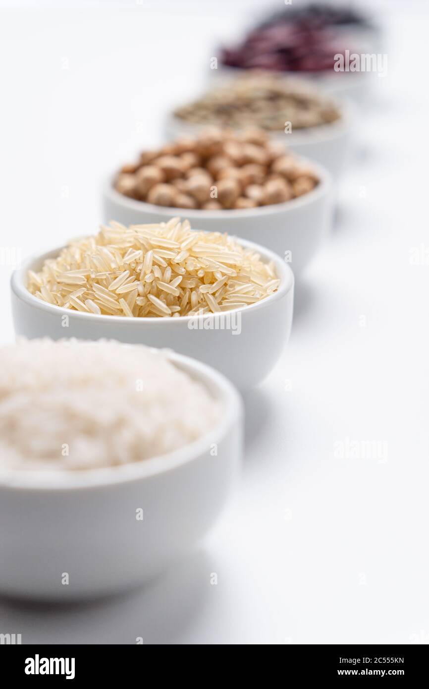 Riso Basmati chiodo di garofano lungo. Profondità di campo poco profonda sui grani di riso basmati in una ciotola bianca con altri tipi di cereali di riso e legumi di fagioli sfocati Foto Stock