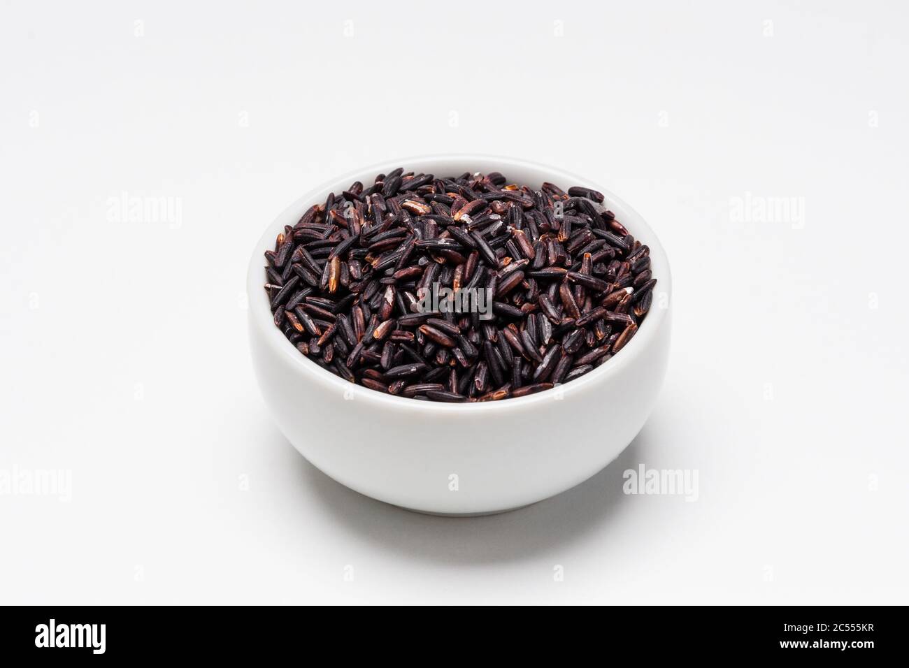 Ciotola di riso nera su sfondo bianco. Il riso proviene da semi di erba, è l'ingrediente di alimento di base più consumato. Il riso nero è un tipo di glutinoso Foto Stock