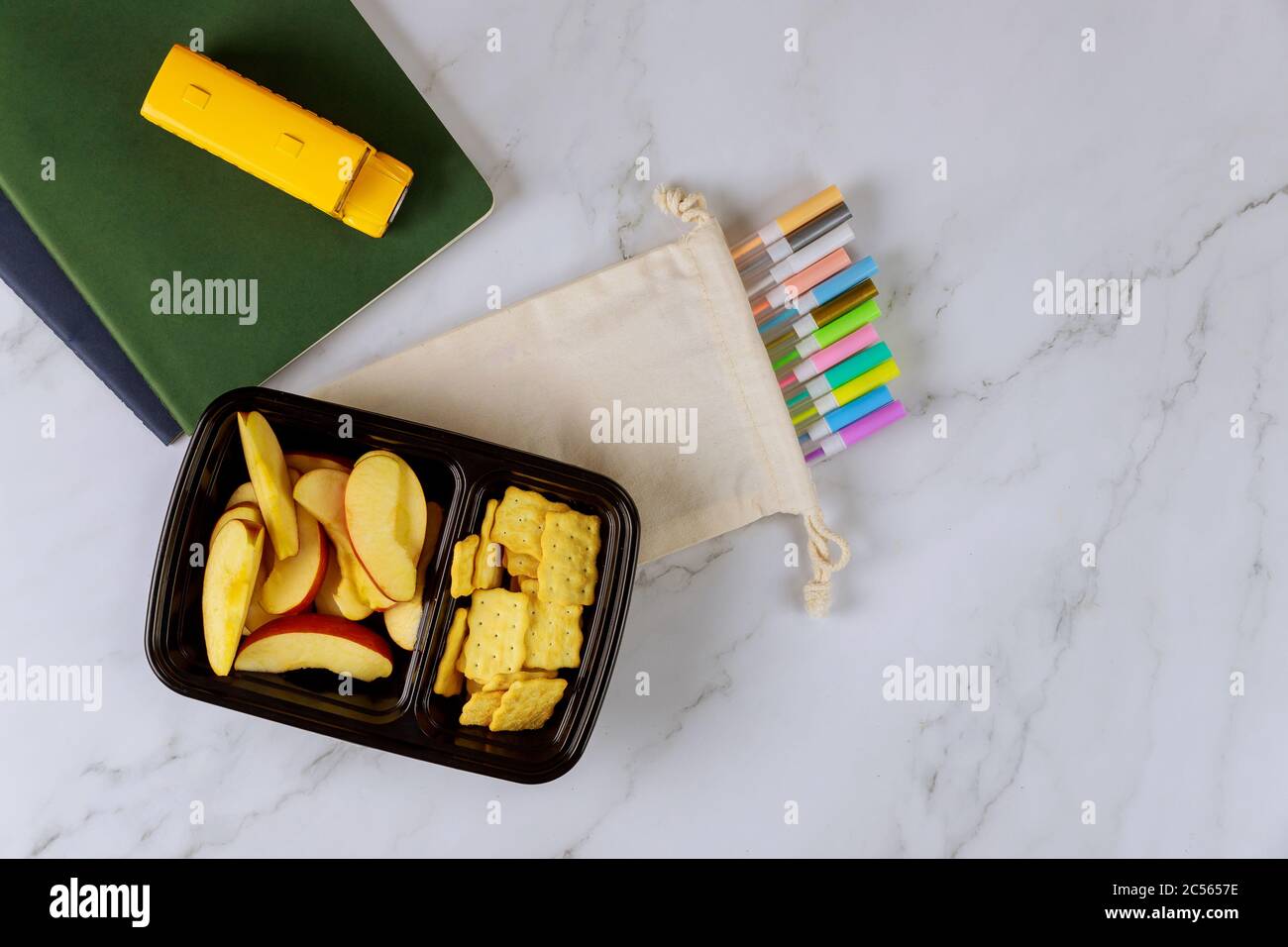 Forniture scolastiche e pranzo al sacco con mele a fette, cracker. Concetto di ritorno a scuola. Foto Stock