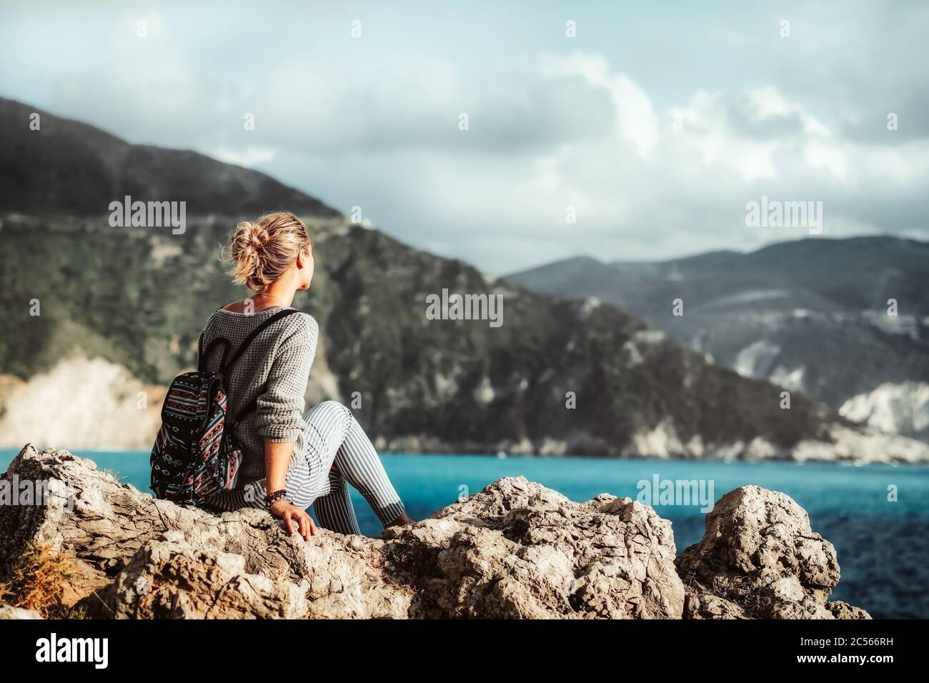 Femmina che si trova sulla costa rocciosa godendo il mare e la costa dell'isola di Cefalonia, Grecia. Foto Stock