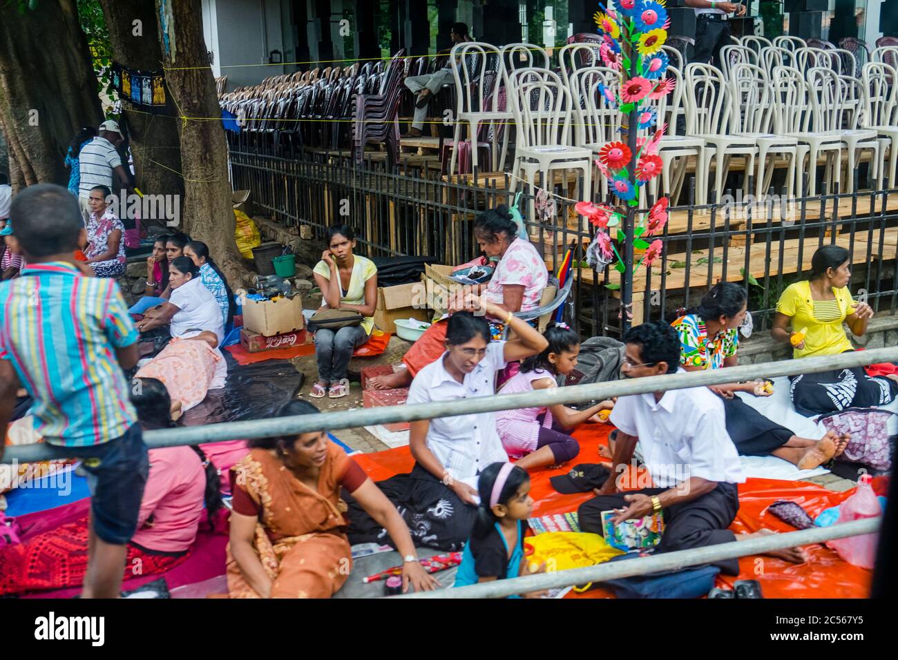 Molte persone si siedono su coperte sul pavimento di fronte a pile di sedie, Sri Lanka Foto Stock