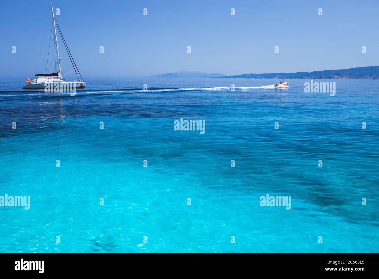 Vacanza. Laguna blu azzurro con onde calme e catamarano a vela con barca a vela con costa sullo sfondo. Foto Stock