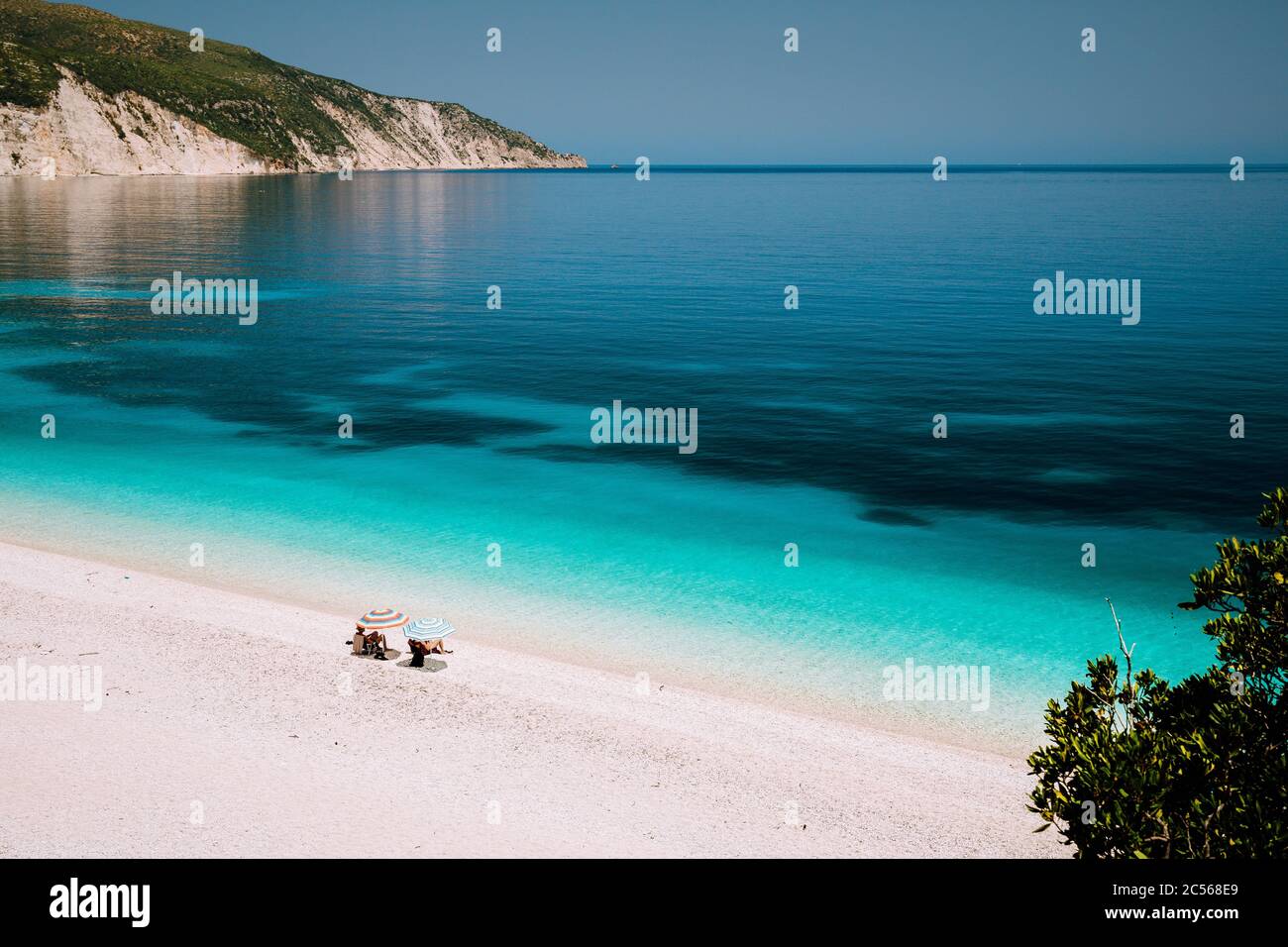 Spiaggia di Fteri, Cefalonia, Grecia. Vacanze estive. Coppia turistica solitaria e irriconoscibile che si nasconde dall'ombrellone relax vicino limpido blu eme Foto Stock