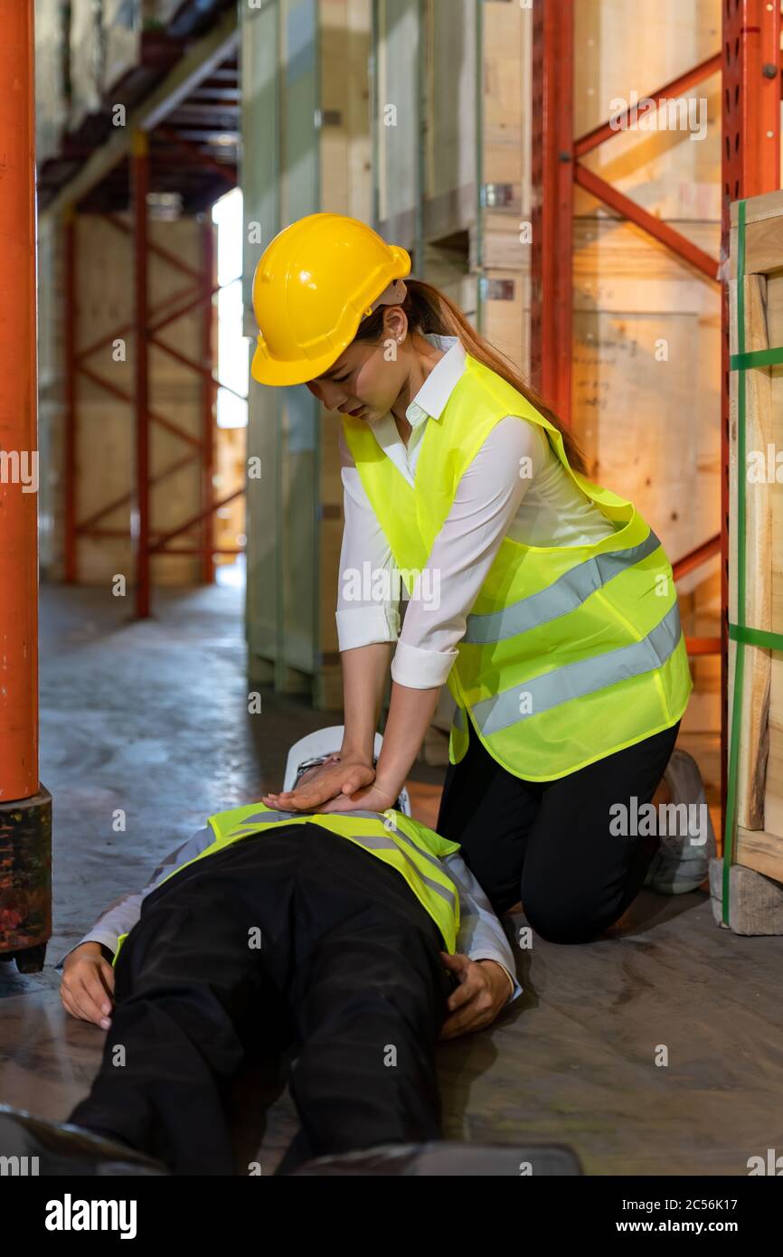 Il lavoratore asiatico esegue la rianimazione cardiopolmonare CPR dopo che il responsabile del magazzino si trova sul pavimento del magazzino dopo un incidente dal carrello elevatore. Uso per la sicurezza Foto Stock