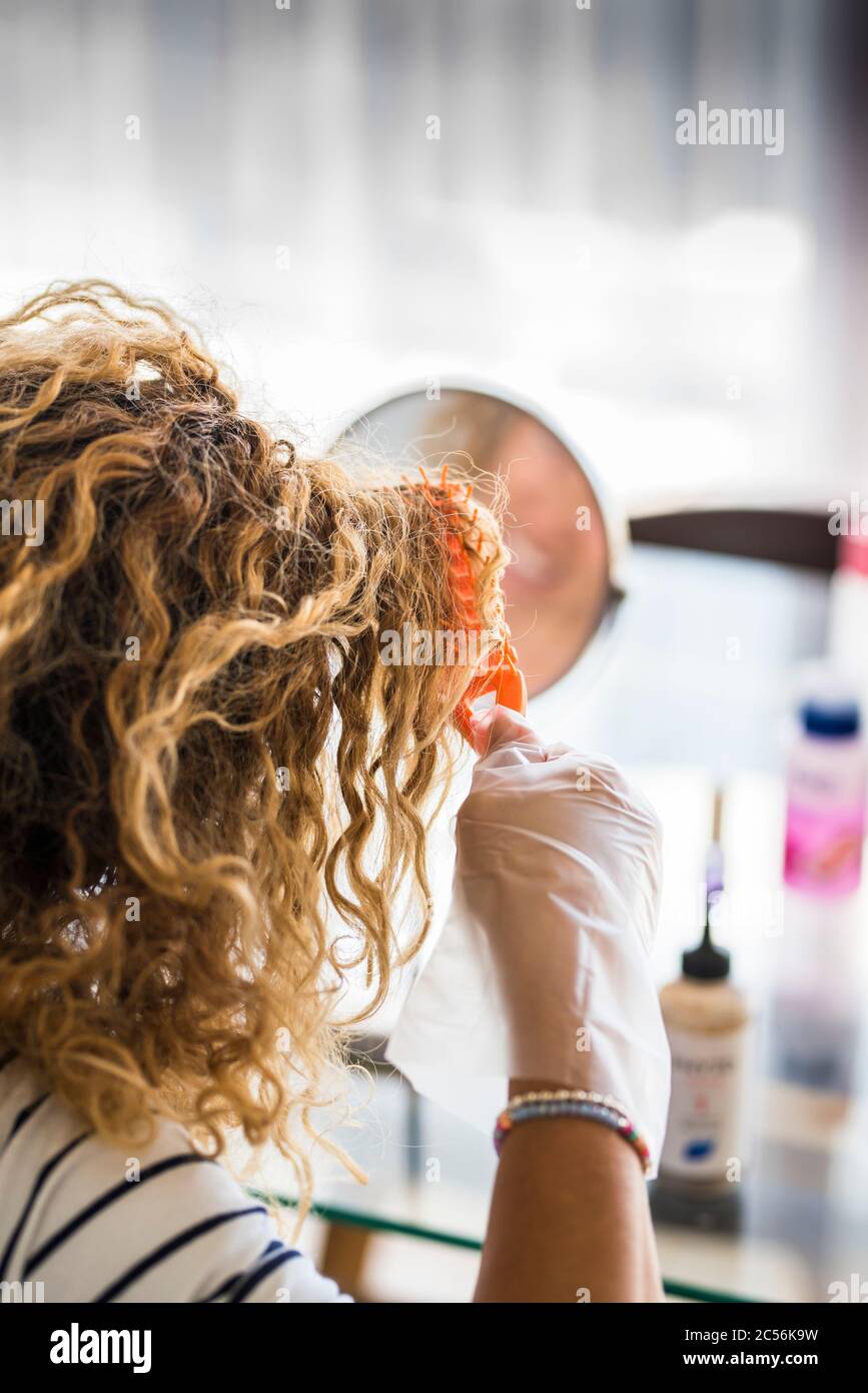 Lavoro femminile irriconoscibile sui suoi lunghi capelli biondi con tintura per colorare e rendere più giovani - persone con prodotti di bellezza a casa - soggiorno a casa concetto per Foto Stock