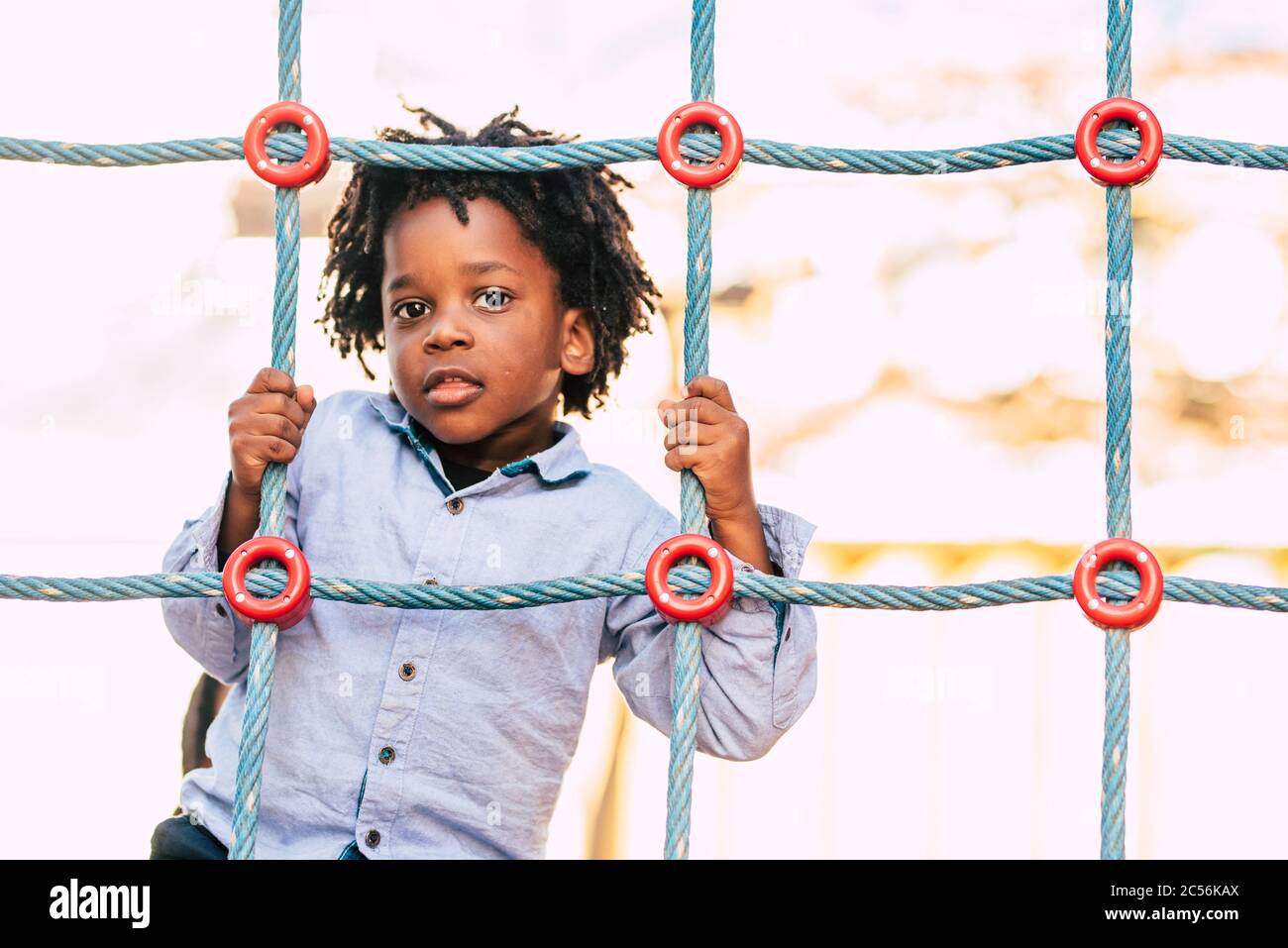Felice e bella giovane capretto nero razza africana con etnico alternativo capelli giocare in un parco giochi con corde colorate e divertirsi Foto Stock