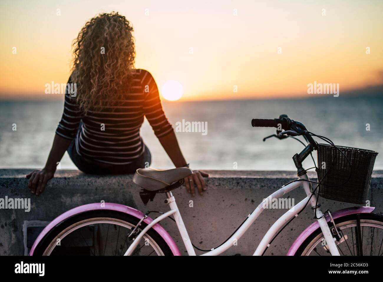 Le persone che amano l'attività all'aperto guardando un bellissimo tramonto colorato - donna con lunghi capelli biondi ricci vista dal retro godersi il relax dopo Foto Stock