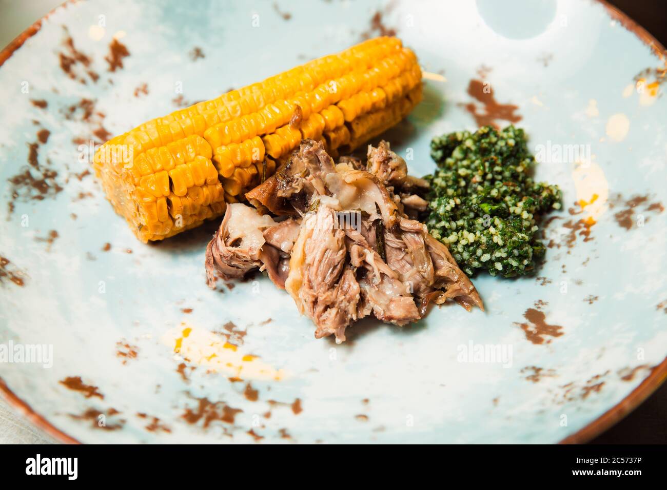 Sulla costata di mais e salsa verde viene servita della carne succosa preparata di fresco. Il cibo si trova su una piastra rotonda. Pronto a servire. Foto Stock