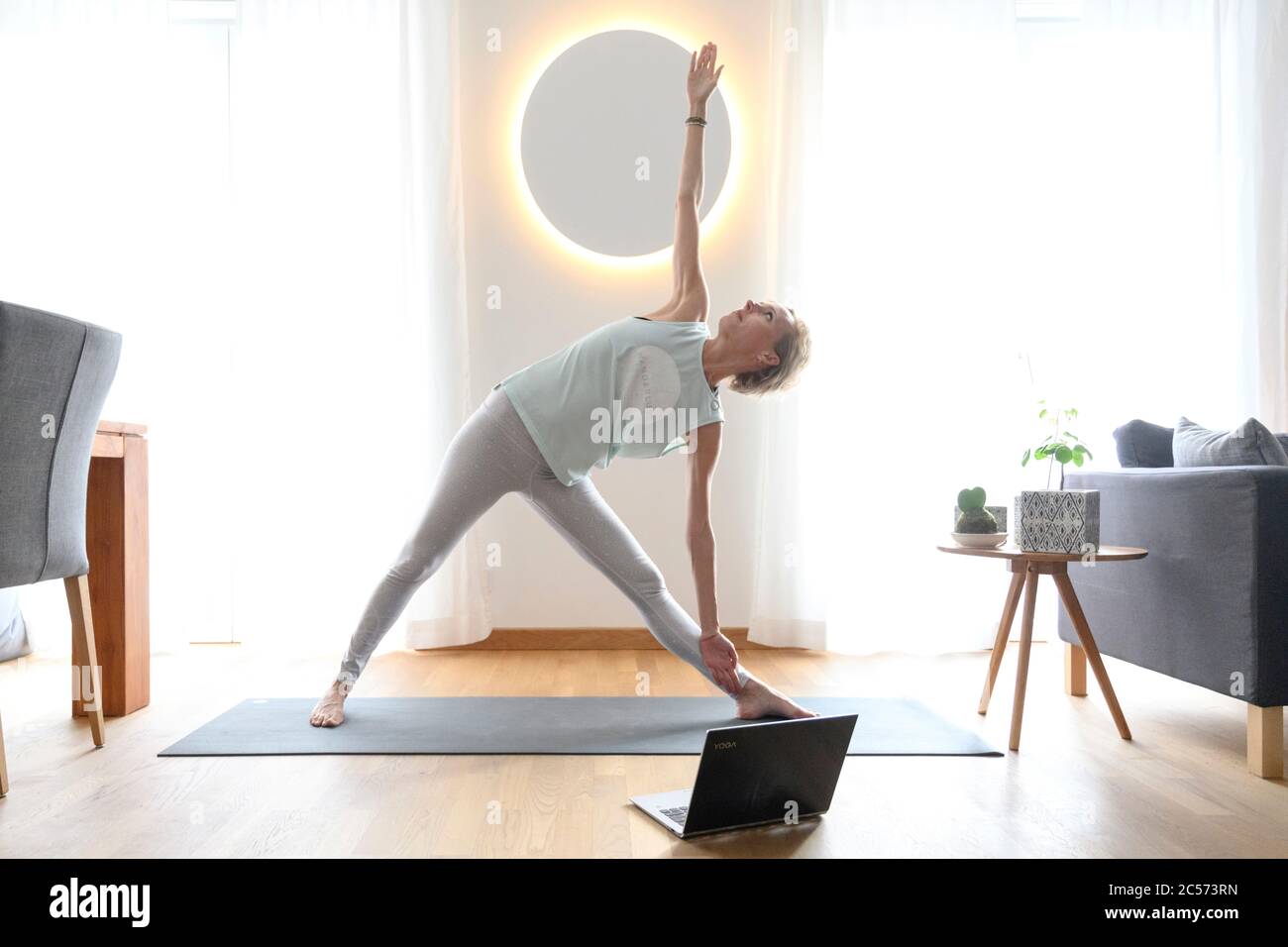 Donna 40+ pratica yoga a casa con notebook. Lezione di yoga online. Foto Stock