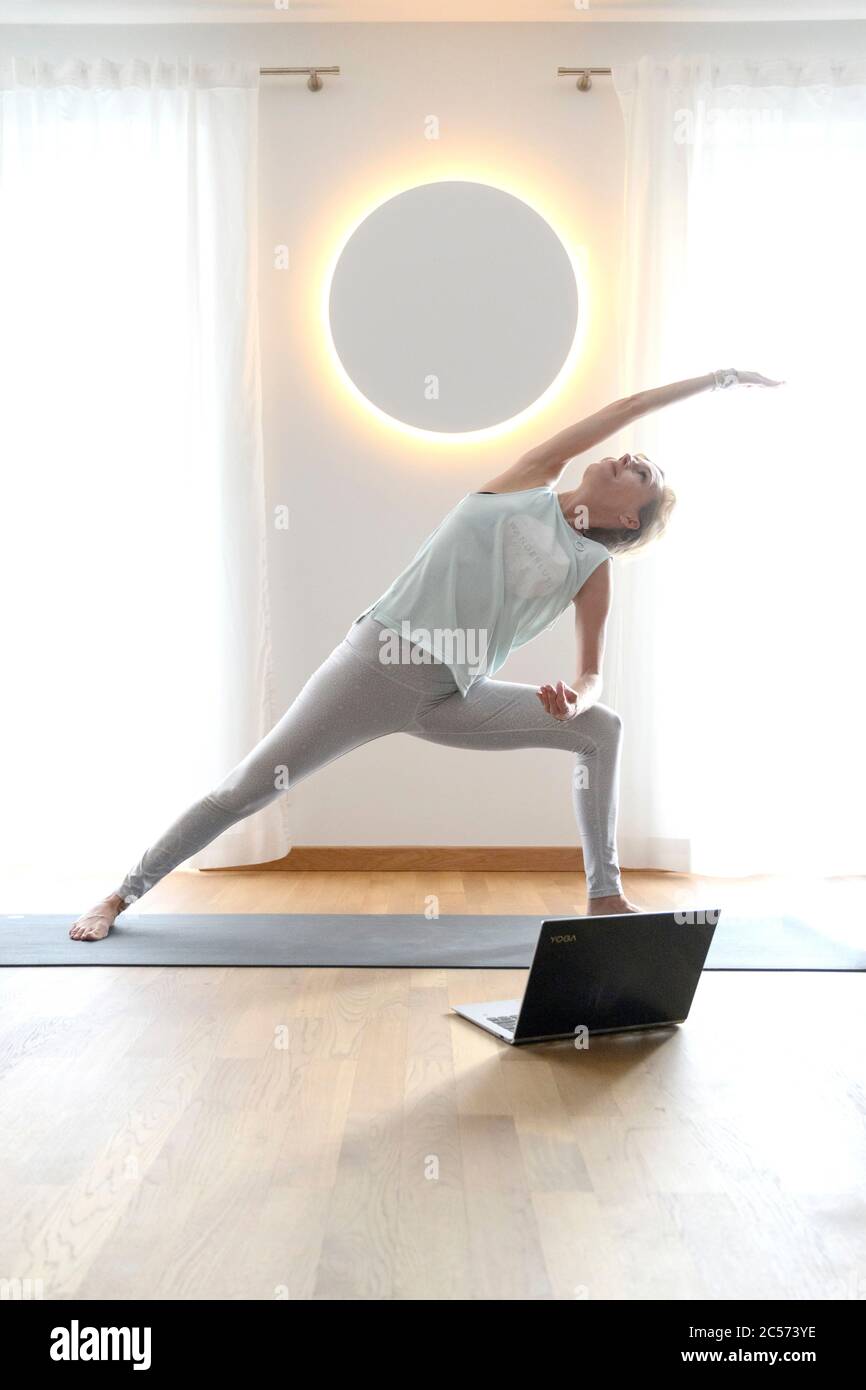 Donna 40+ pratica yoga a casa con notebook. Lezione di yoga online. Foto Stock