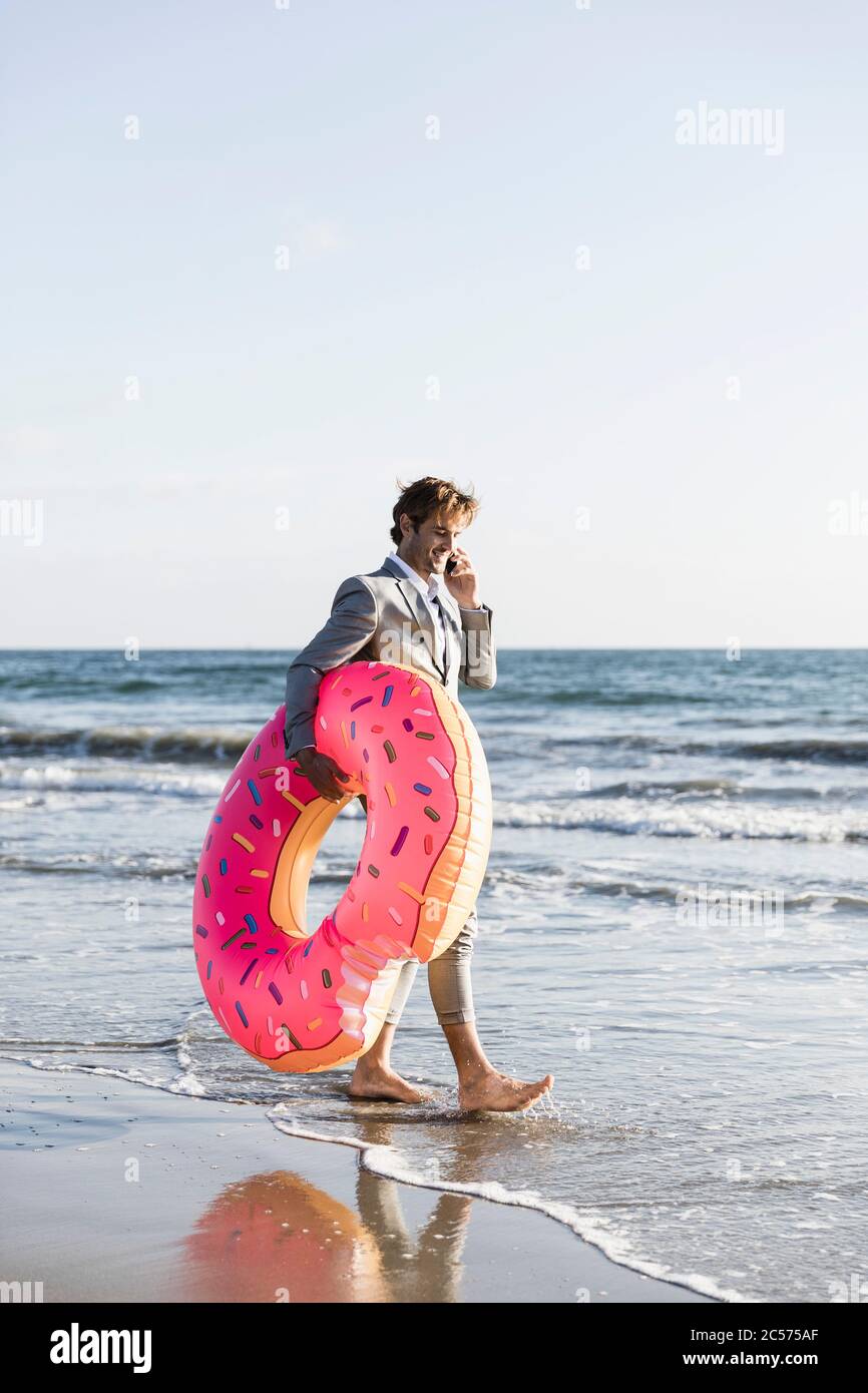 Uomo d'affari con ciambella gonfiabile sulla spiaggia soleggiata dell'oceano, Los Angeles, California Foto Stock
