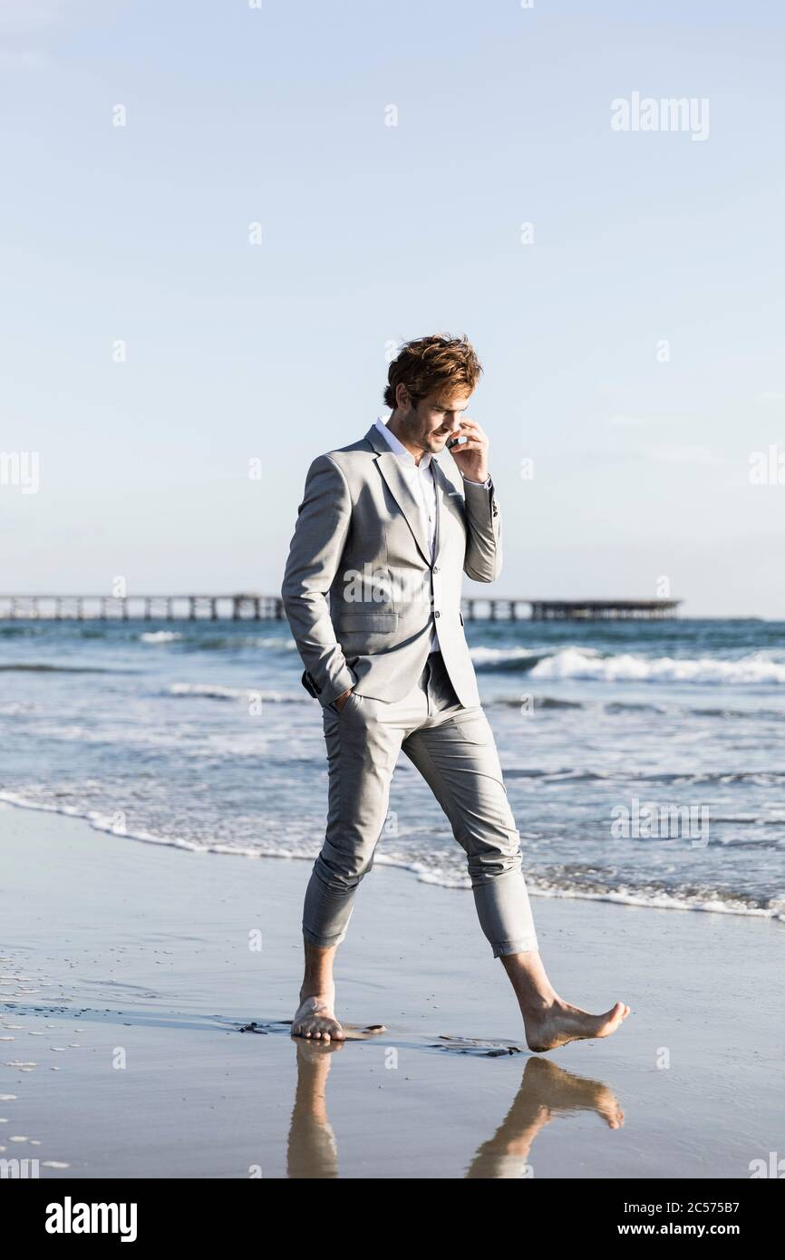 Uomo d'affari a piedi nudi che cammina sulla soleggiata spiaggia dell'oceano, Los Angeles, California Foto Stock