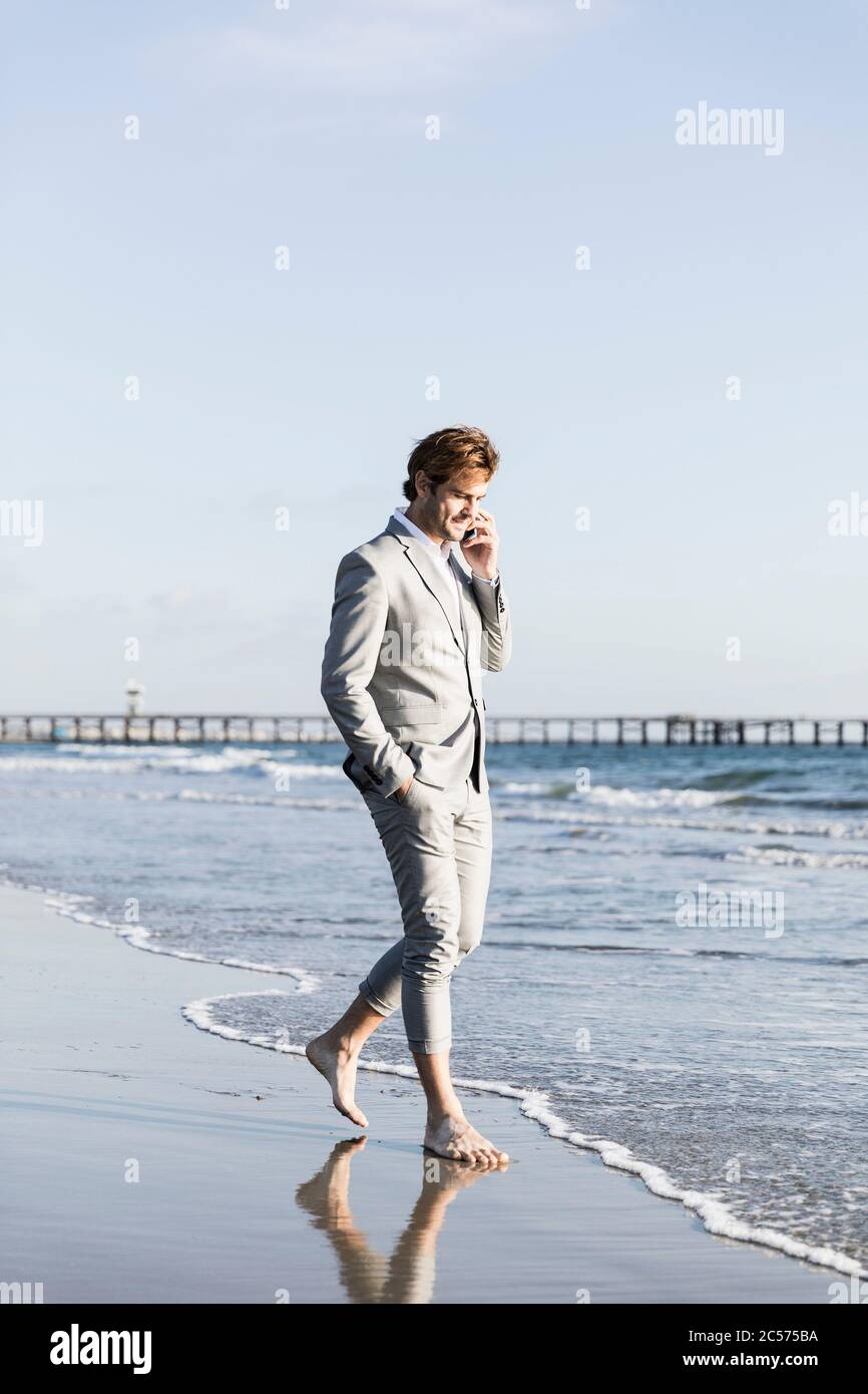 Uomo d'affari Barefoot che parla su smartphone sulla soleggiata spiaggia dell'oceano, Los Angeles, California Foto Stock