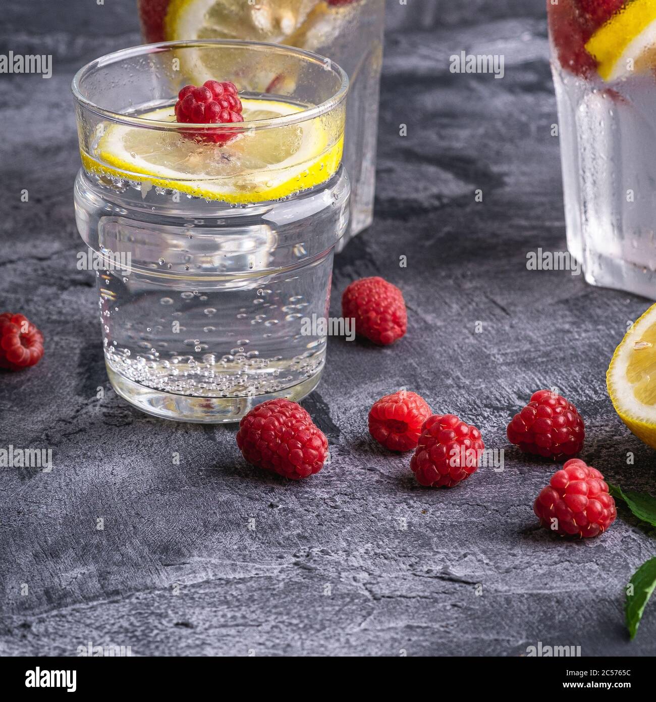 Bevanda fresca di acqua ghiacciata con limone, frutta di lamponi e foglia di menta in vetro su fondo di pietra calcestruzzo, dieta estiva bevanda, angolo vista selectiv Foto Stock