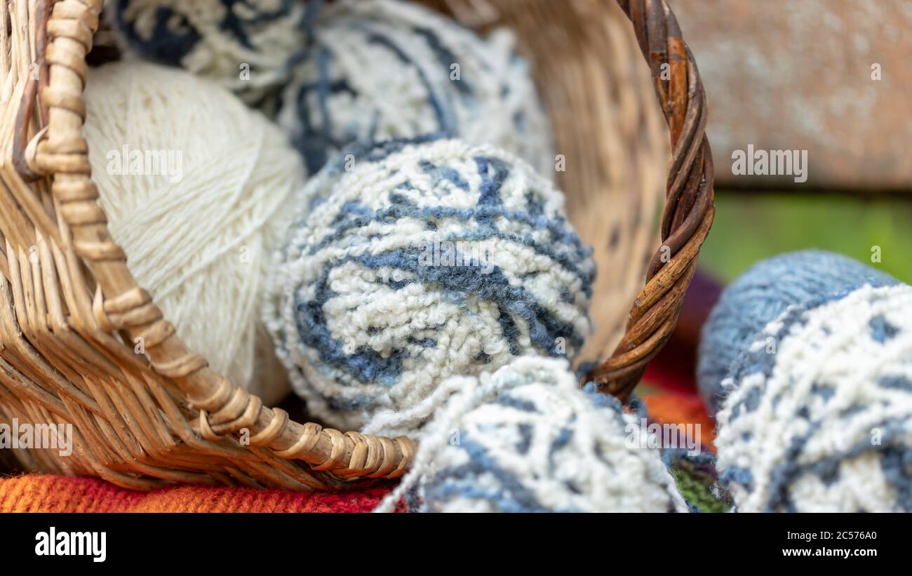 palline di lana blu e bianca in un cesto di vimini su una coperta di maglia multicolore. Sfondo naturale. Poster orizzontale con spazio per la copia. Filato per maglia Foto Stock