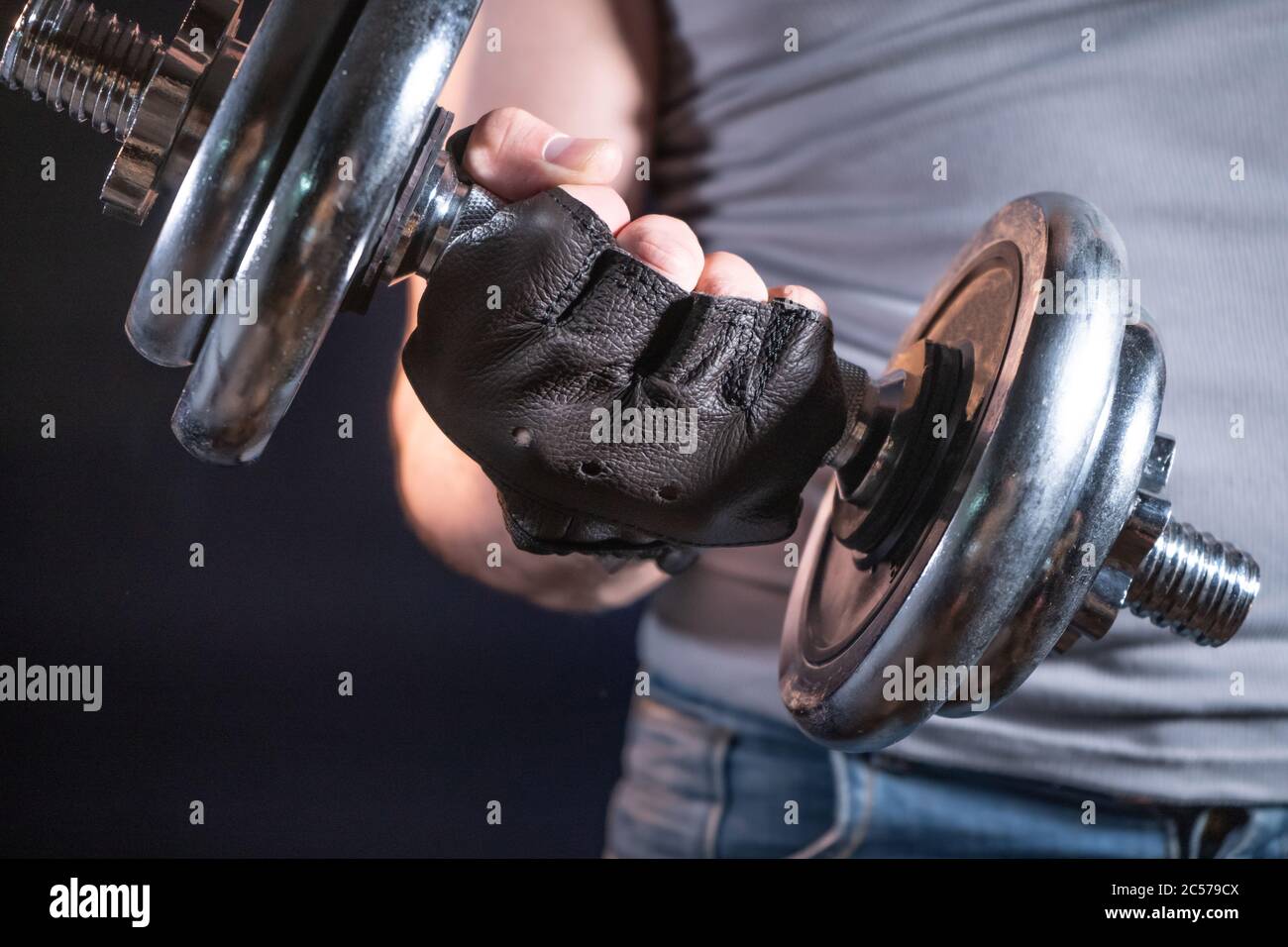 Uomo forte in guanti sportivi con manubri Foto Stock