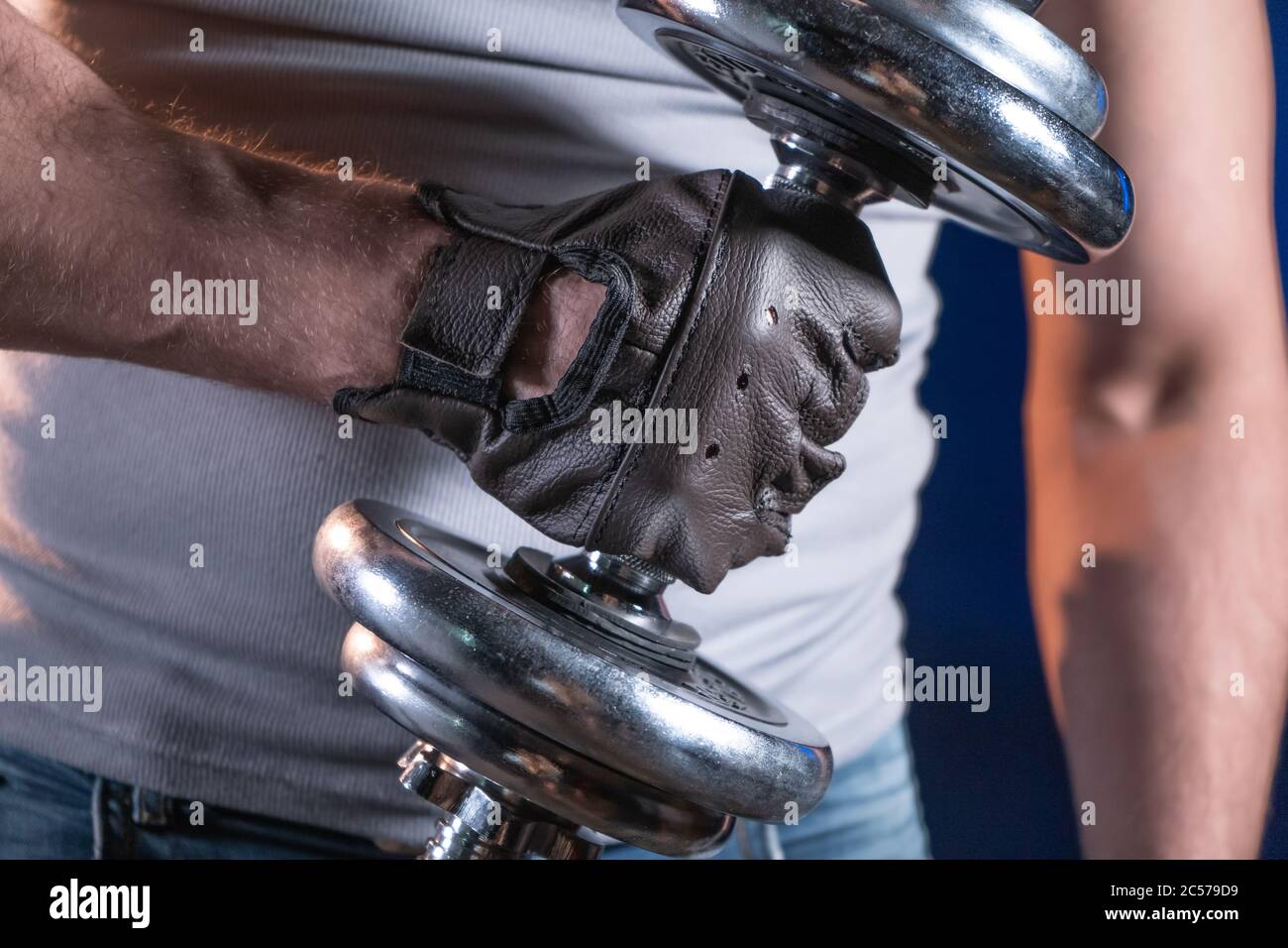 Uomo forte in guanti sportivi che reggono il manubri Foto Stock