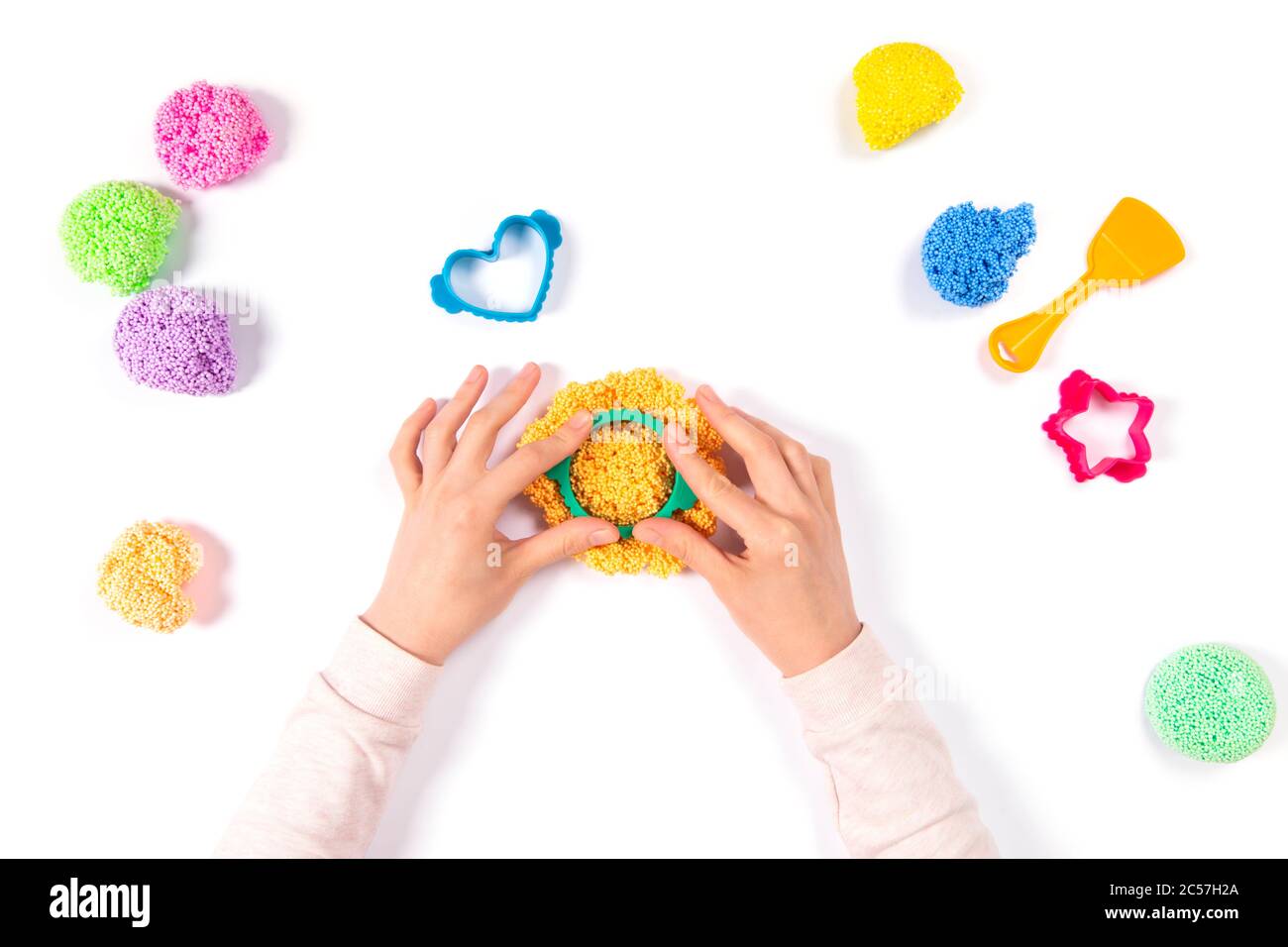 Ragazza che gioca playfoam a casa isolato su sfondo bianco. Vista dall'alto. Gioco di formazione domestica con argilla. Concetto di fai da te per lo sviluppo iniziale. Le mani giocano con la mo Foto Stock