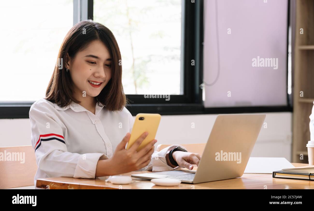 La ragazza asiatica lavora da casa o uno studente sta studiando da casa o da un freelance. Utilizza uno smartphone e un computer portatile Foto Stock