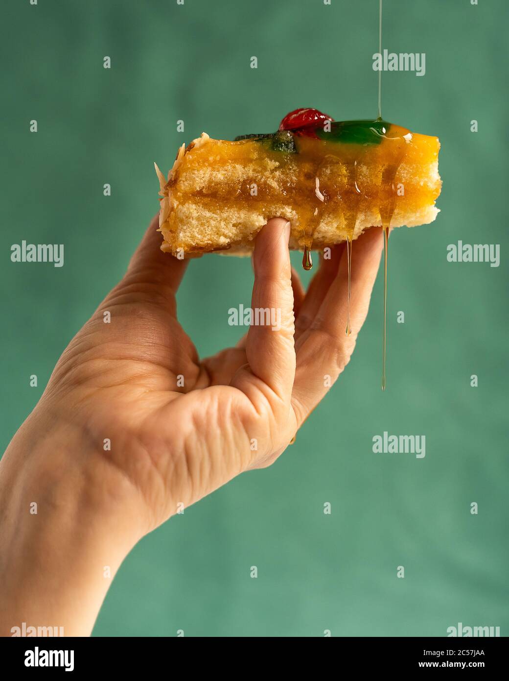 Foto verticale di una mano con una torta con frutta caramellate mentre si aggiungono caramelle liquide che danno via la torta con lo sfondo verde Foto Stock