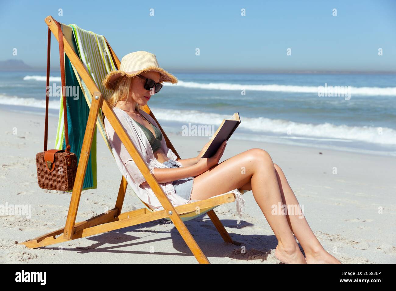 Donna che legge un libro mentre si siede sulla spiaggia Foto Stock