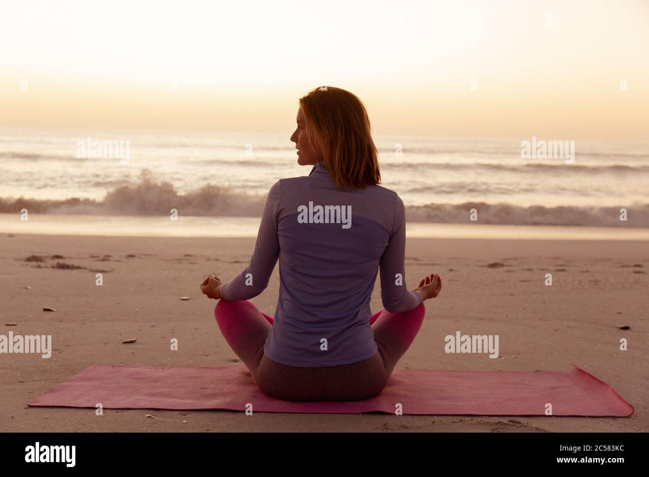 Vista posteriore della donna che esegue yoga sulla spiaggia durante il tramonto Foto Stock