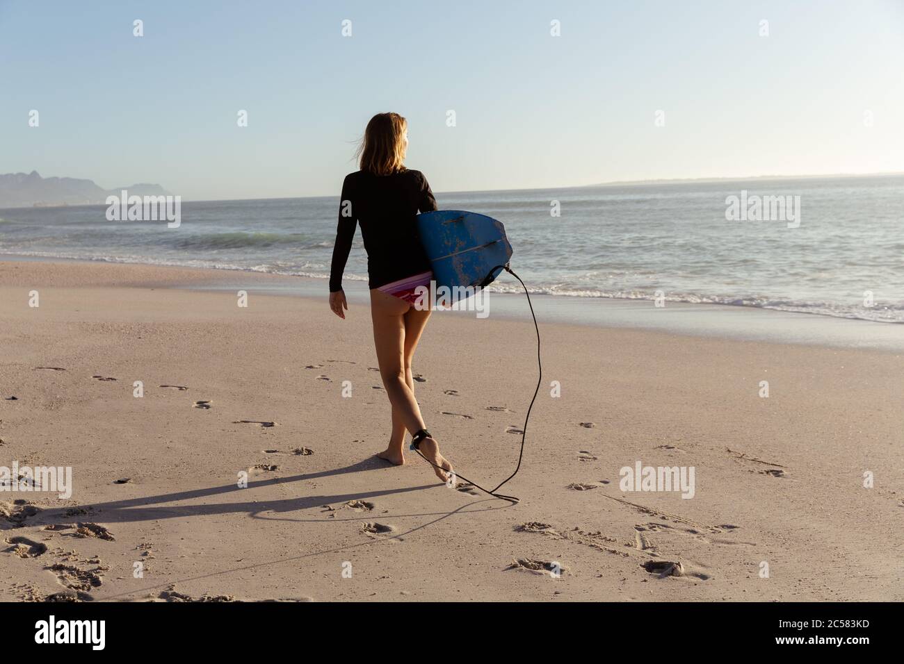 Donna con la tavola da surf di camminare sulla spiaggia Foto Stock