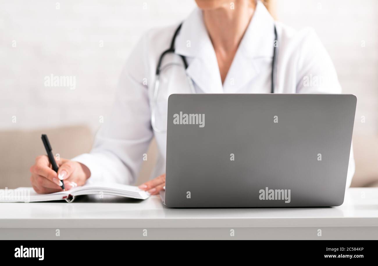 Consultazione medica online. Donna in camice bianco fa note con penna e notebook Foto Stock