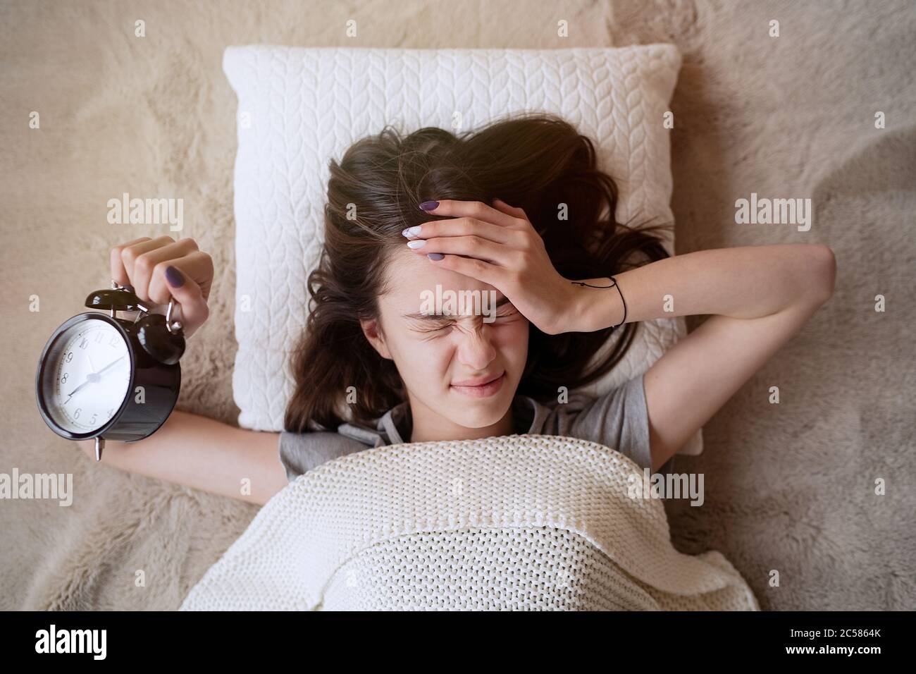 Sonnolenta adolescente che spegne l'allarme al mattino mentre si sdraia a letto Foto Stock