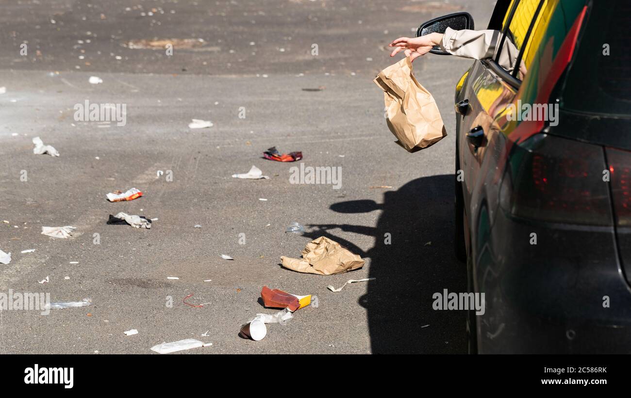 Donna che tiene in mano il sacchetto di carta dei rifiuti, fuori dal finestrino che guida in auto. Autista che getta rifiuti nel parcheggio. Inquinamento ambientale Foto Stock