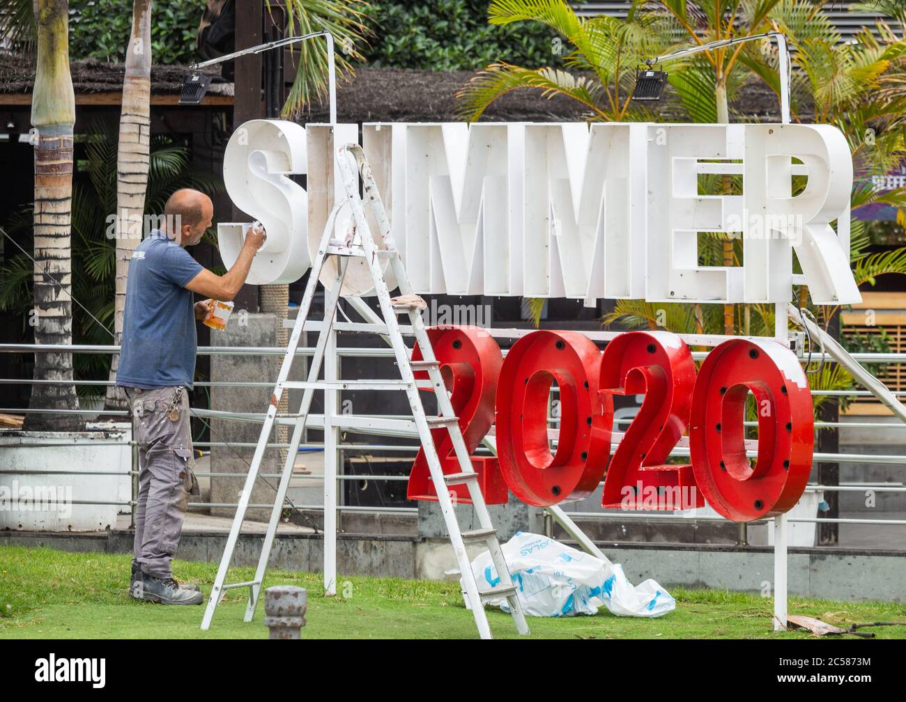 Las Palmas, Gran Canaria, Isole Canarie, Spagna. 1 luglio 2020. Un uomo dipinge un cartello estivo 2020 fuori da un bar sulla spiaggia che si affaccia su una spiaggia turistica libera della città a Las Palmas sulla Gran Canaria. Con i principali tour operator del Regno Unito che non devono iniziare i voli per Gran Canaria fino a metà luglio, molti hotel rimangono chiusi. Con le isole Canarie una delle province meno colpite della Spagna durante la pandemia di Coronavirus, la gente del posto è ansiosa di vedere il ritorno dei turisti, poiché circa il 40% della popolazione delle isole Canarie dipende dal turismo per l'occupazione. Credit: Alan Dawson/Alamy Live News. Foto Stock