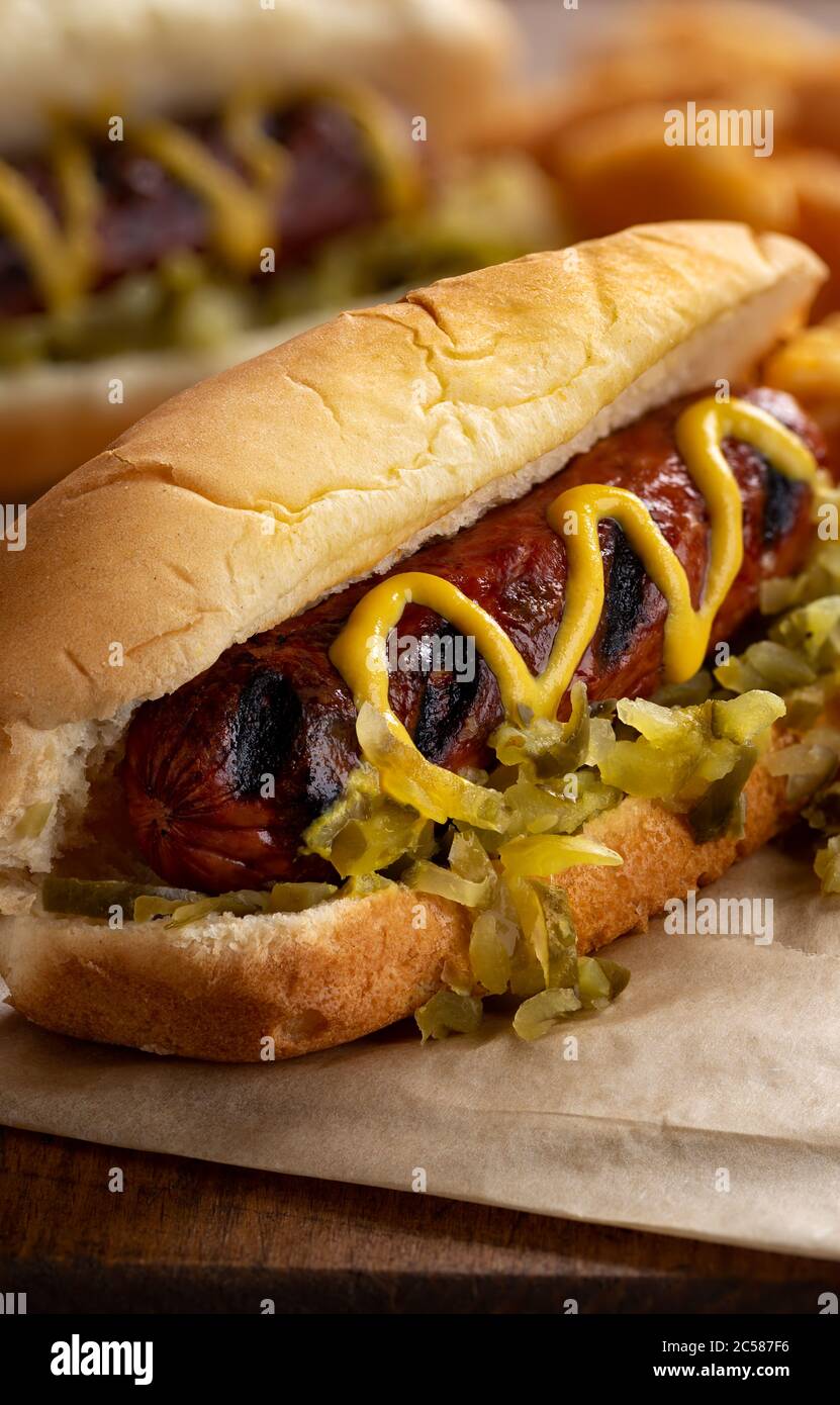 Cane caldo alla griglia con senape e gustare su un panino e patatine fritte su una tavola rustica di legno Foto Stock