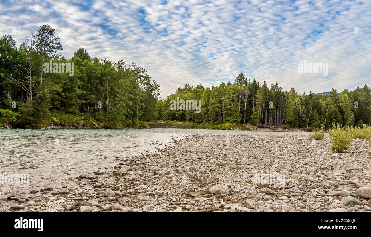 Tramonto sull'alto fiume Kitimat nella Columbia Britannica Settentrionale, Canada, con un cielo blu nuvoloso, boschi confidenti e ghiaia bar. Foto Stock