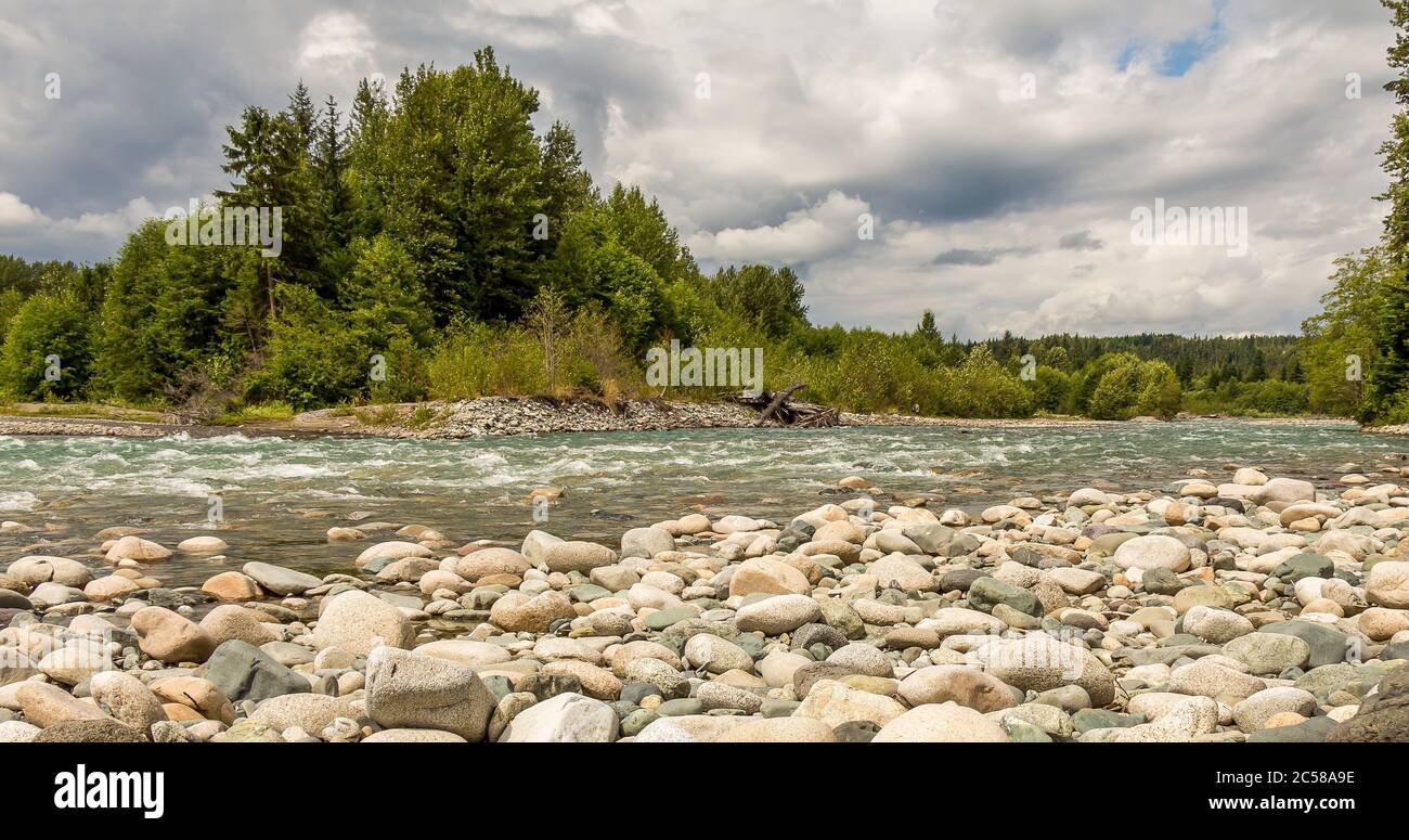 Un masso disseminato, fiume Kitimat veloce che scorre, accanto ad una foresta, in una giornata nuvolosa, nella Columbia Britannica. Foto Stock