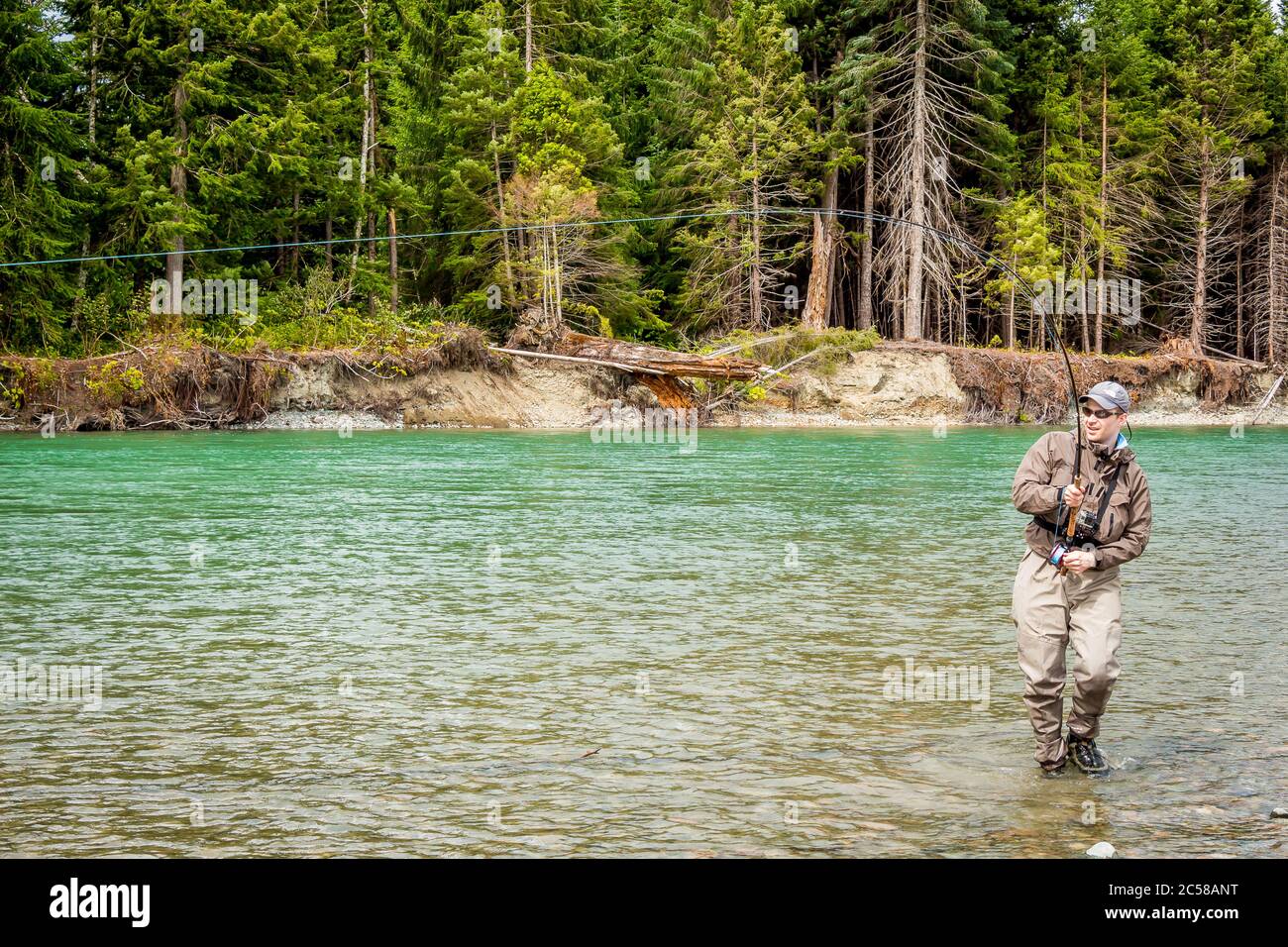 Un pescatore di mosca di sport agganciato in un salmone sul fiume verde di Kitimat, nella Columbia Britannica, Canada, con il bosco di conifere in background. Foto Stock
